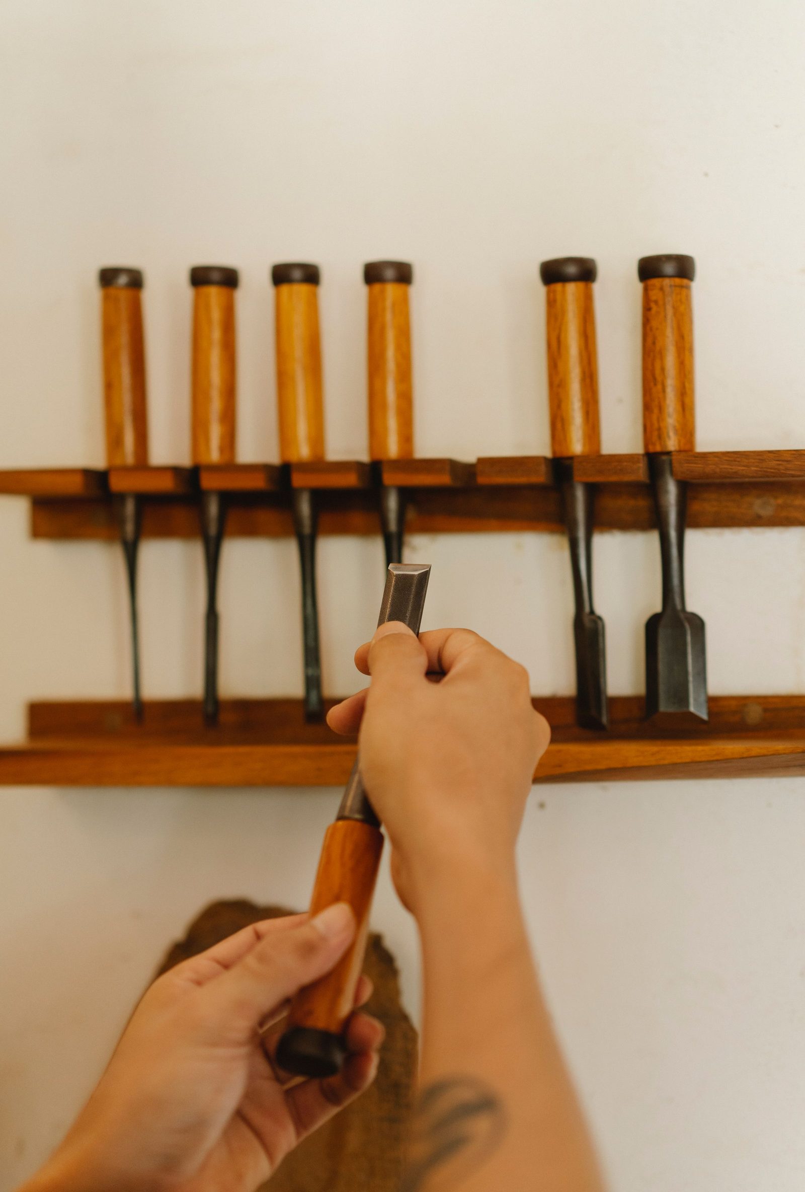 Hands choosing a chisel from a set arranged on a rack in a woodworking studio.