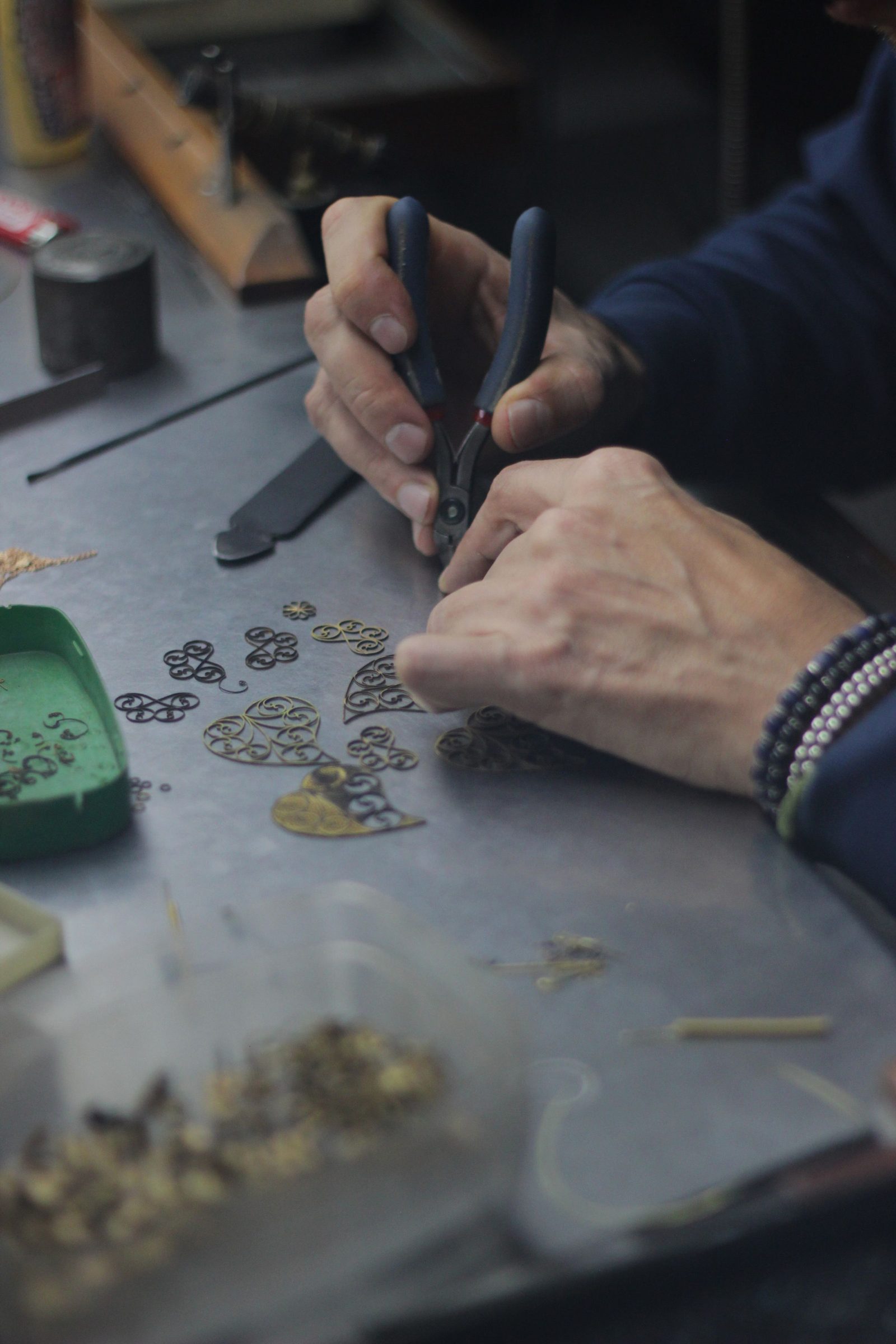 An artisan’s hands shaping a piece of gold jewellery at a workbench.