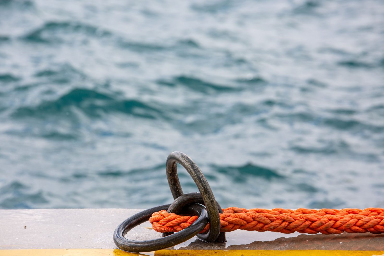 An orange mooring rope tied to a metal ring on a jetty.