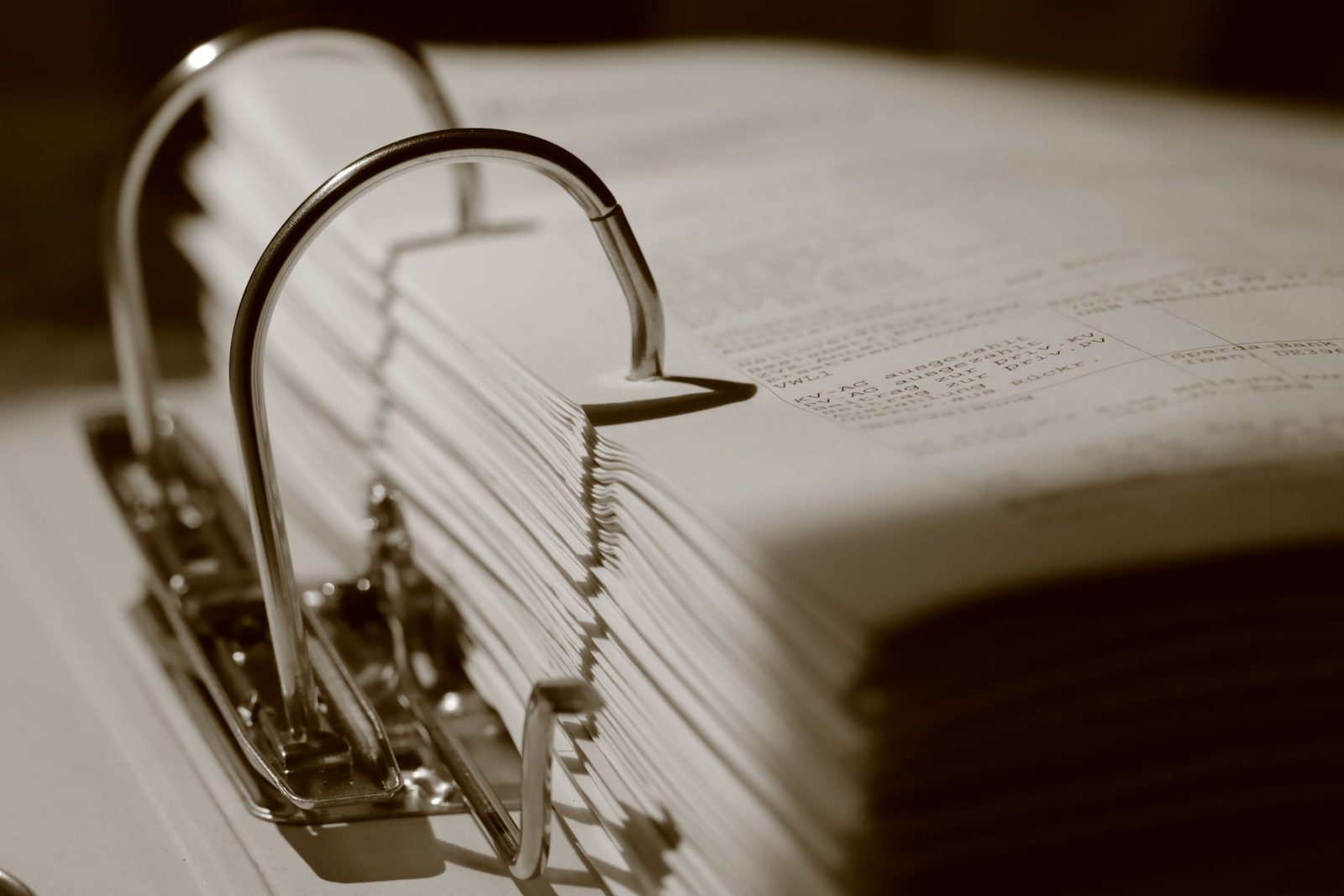 A sepia close-up of a ring binder packed with documents.