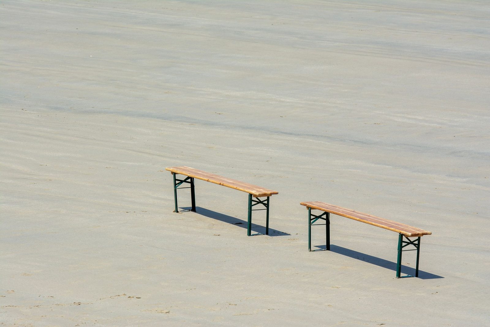 Two plain wooden benches stand side by side on an empty beach.