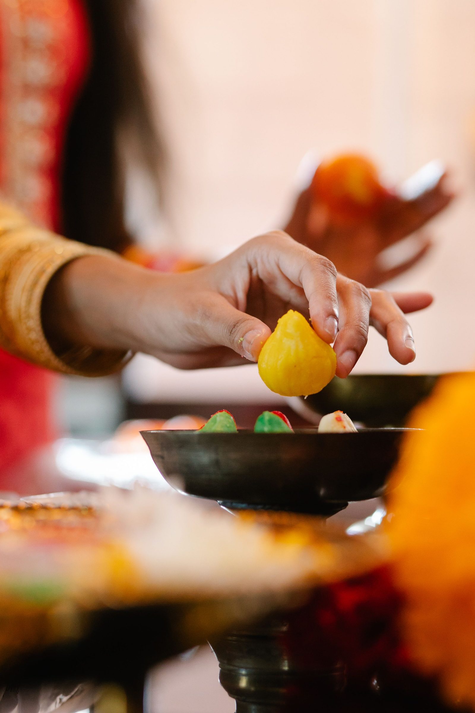 A hand places a yellow Indian sweet into a bowl.