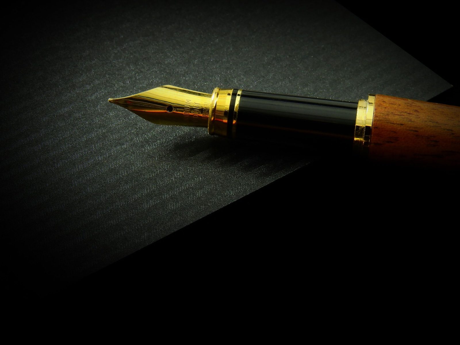 Close-up of a gold fountain pen nib resting on textured black paper.