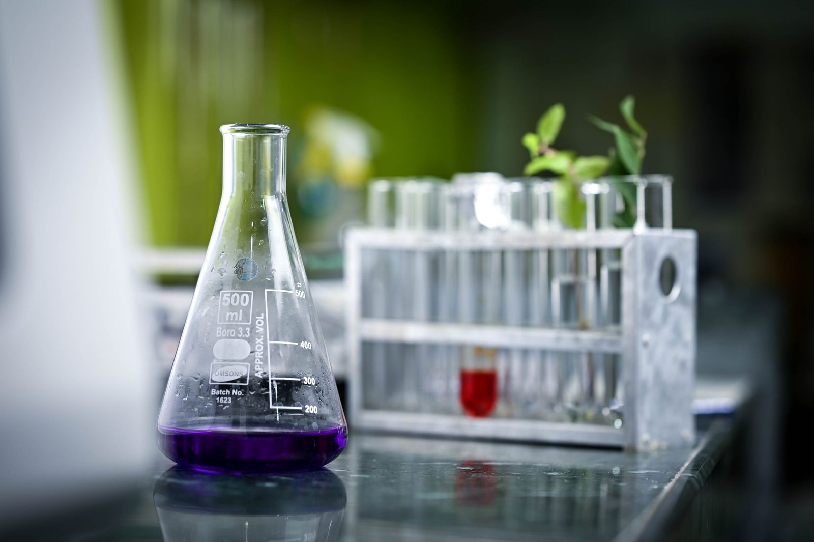 A laboratory flask of purple liquid stands among test tubes on a bench.