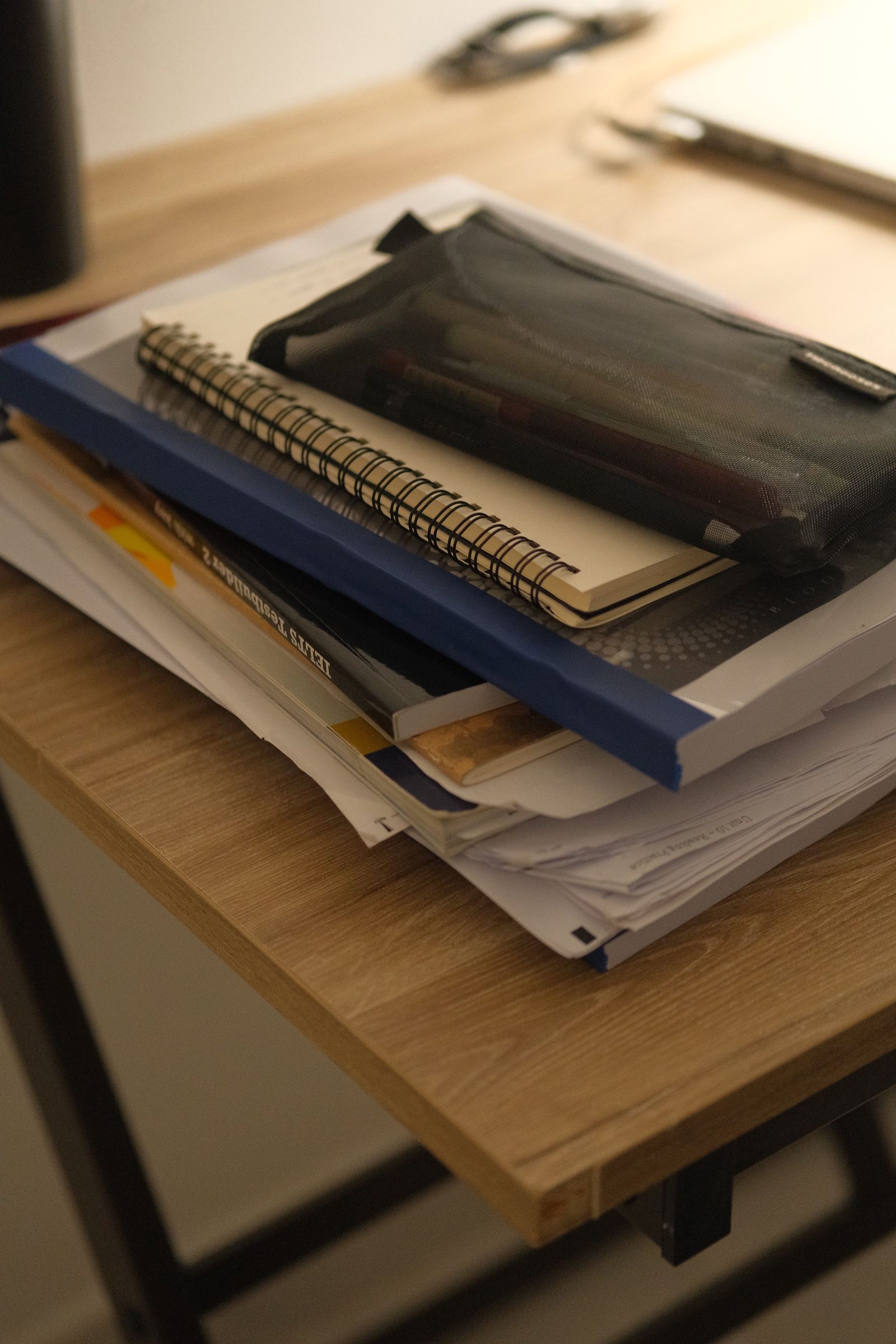A neat stack of notebooks and papers sits beside a pencil case on a wooden desk.