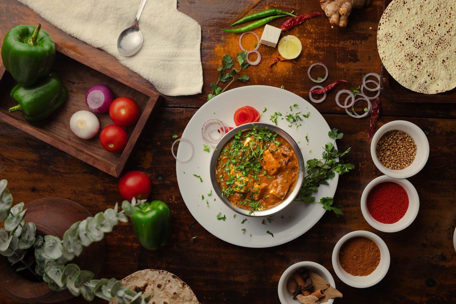 Seen from above an Indian meal of curry and vegetables is laid out among bowls of spices.