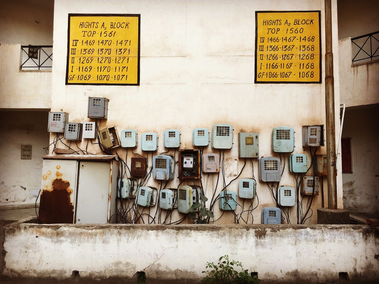 Old electricity meter boxes and tangled wiring on a weathered concrete wall in India.