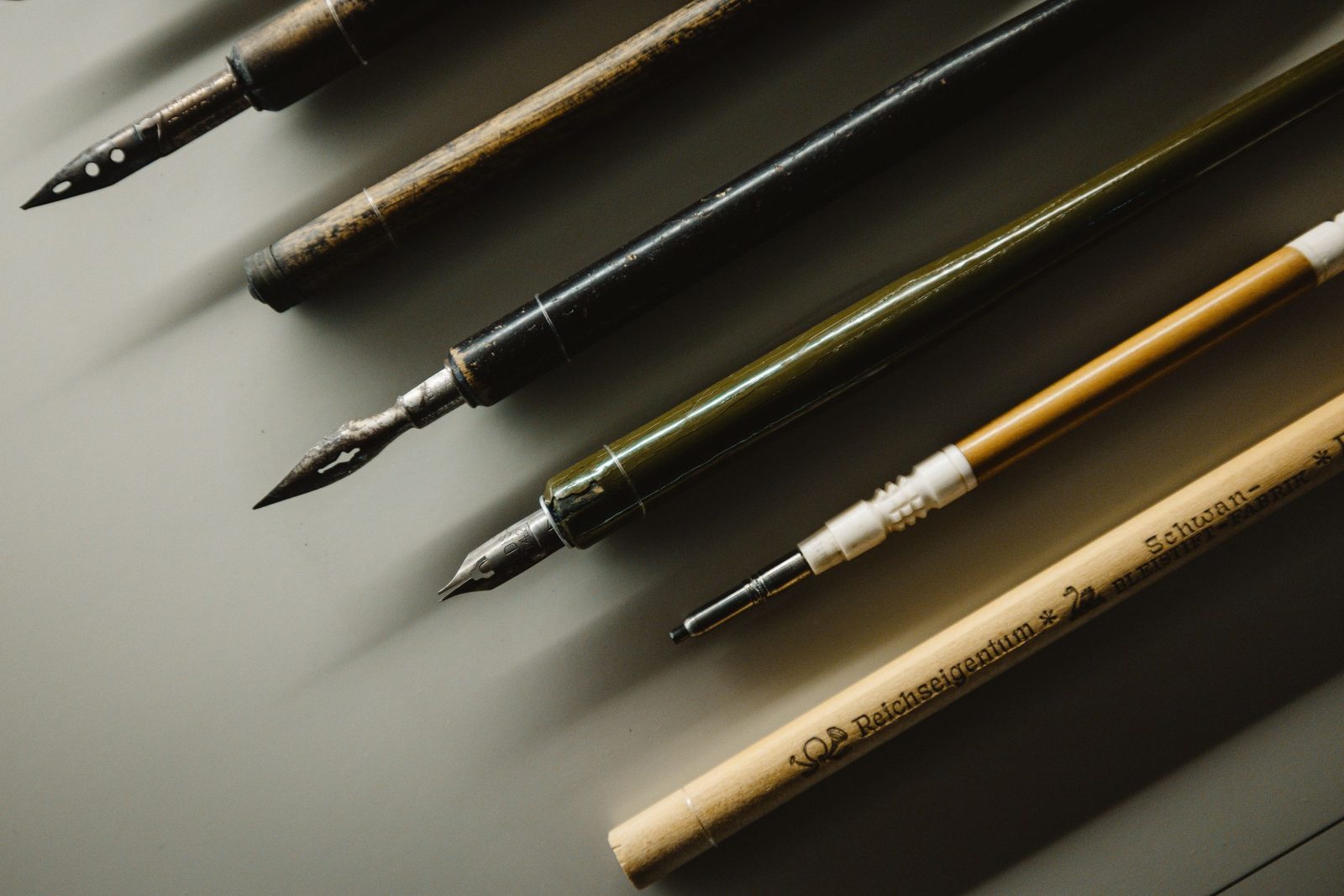 Vintage fountain pens and calligraphy nibs laid out on a wooden desk.