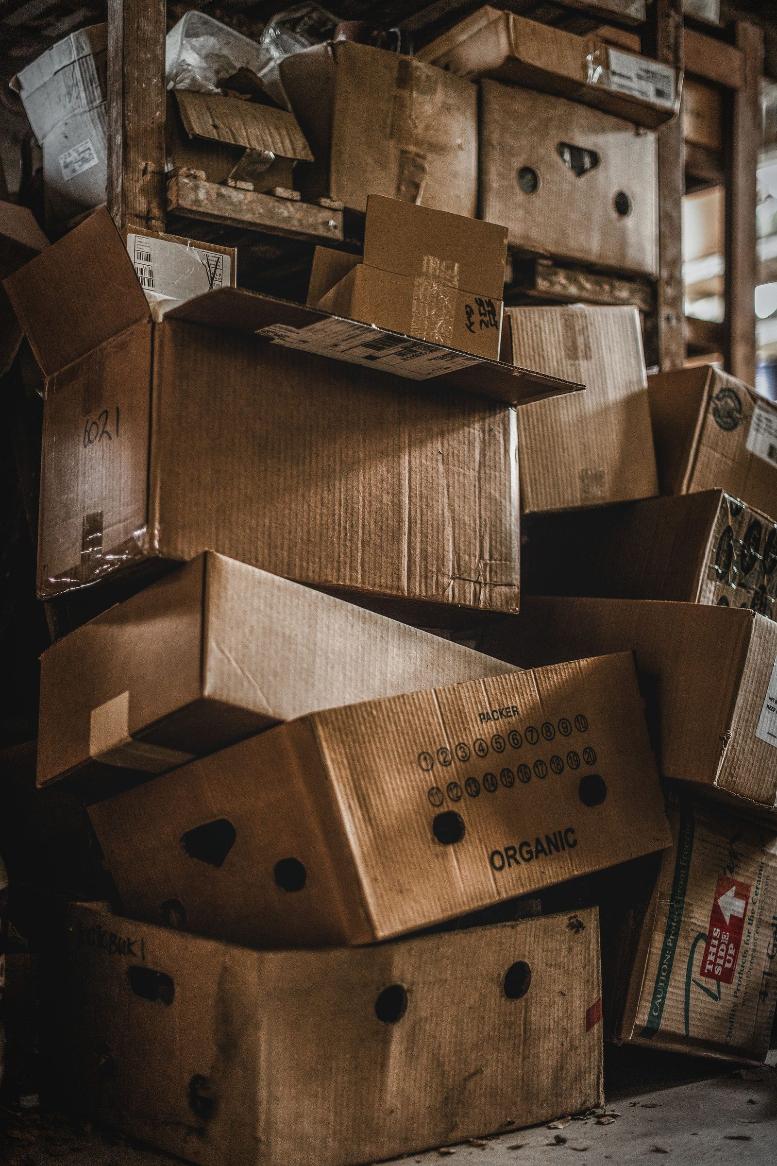 Cardboard boxes of many sizes are piled high inside a cluttered warehouse.