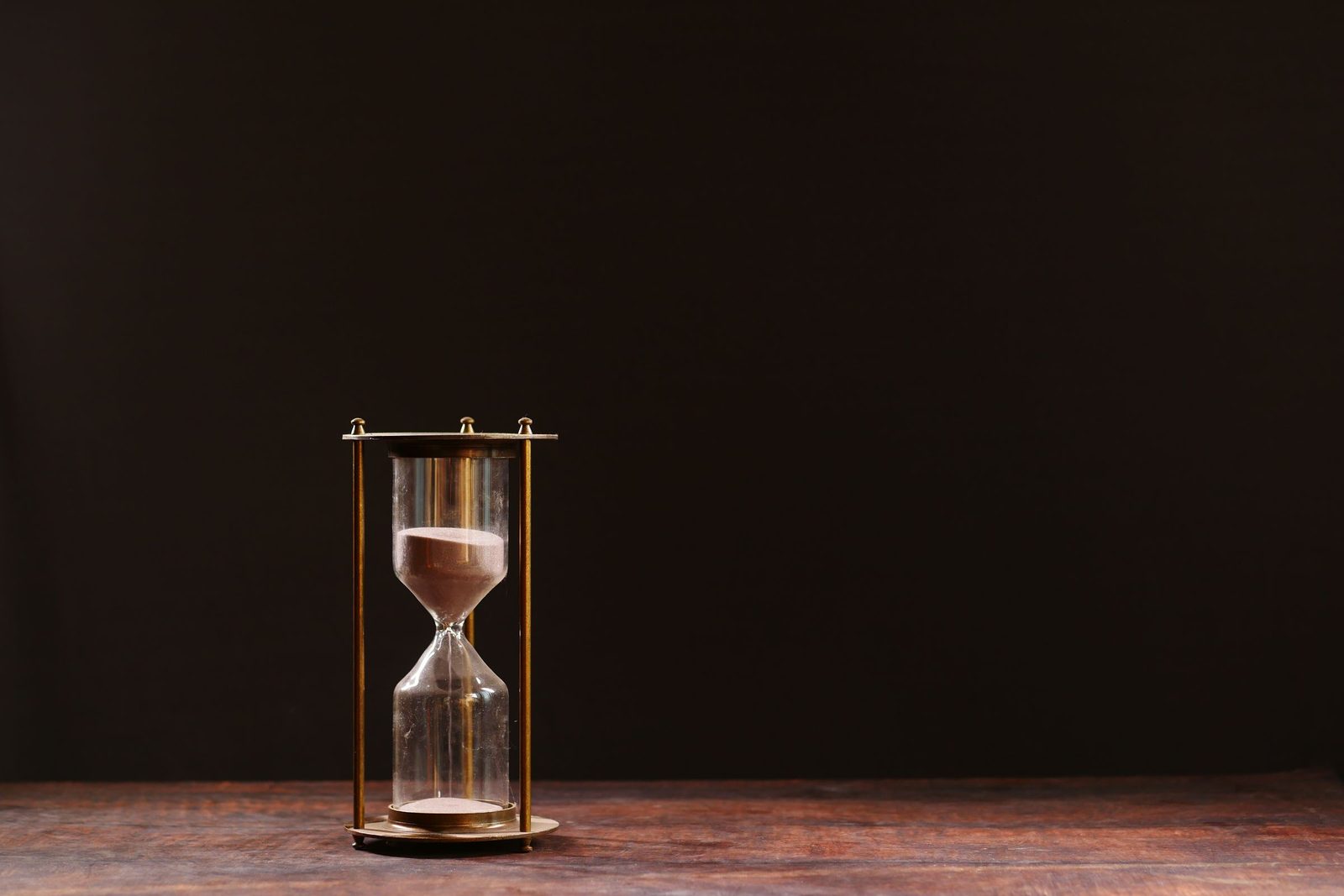 Sand runs through a glass hourglass against a dark background.