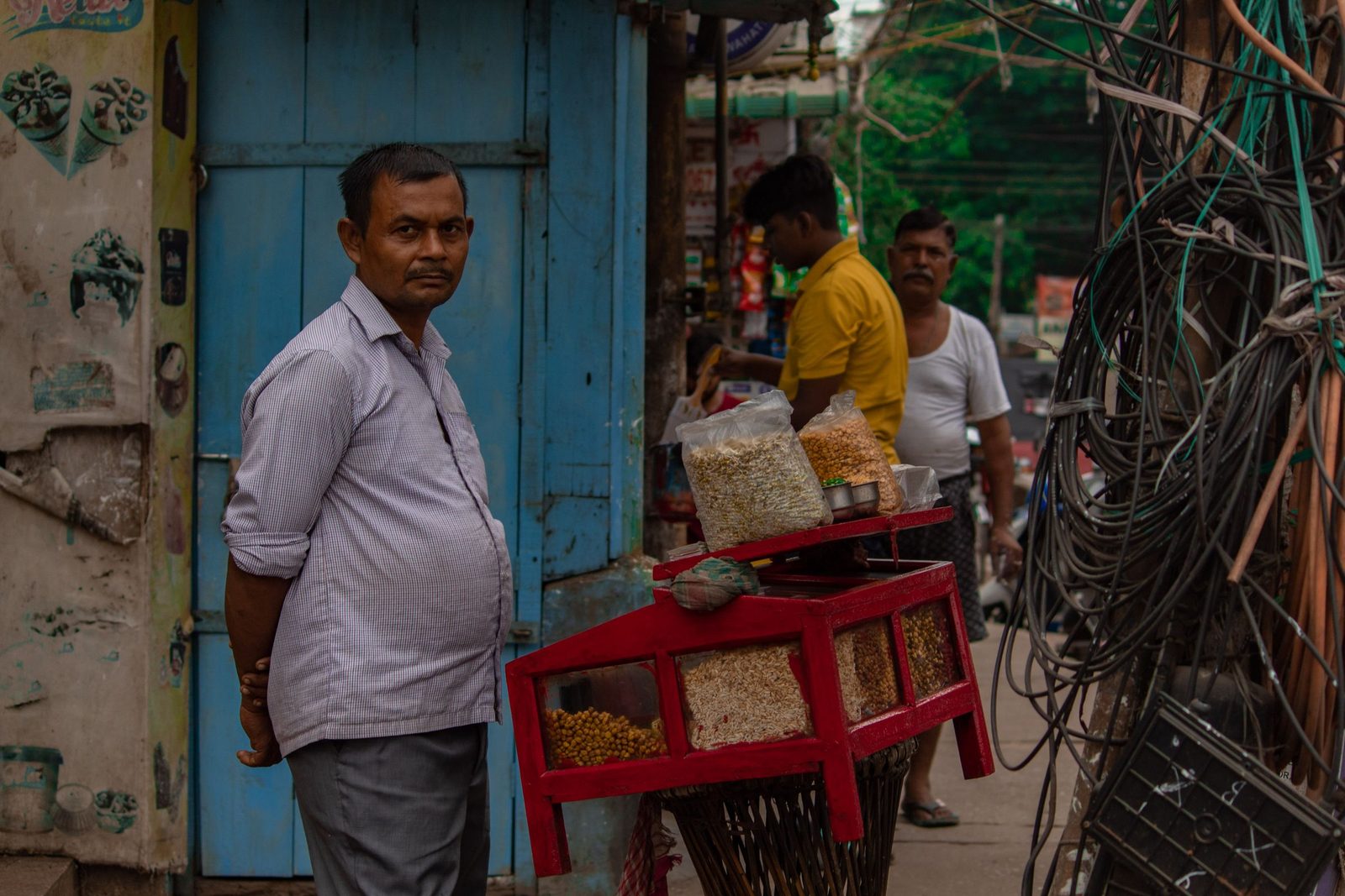 A street vendor stands beside his snack stall in a busy Indian market.