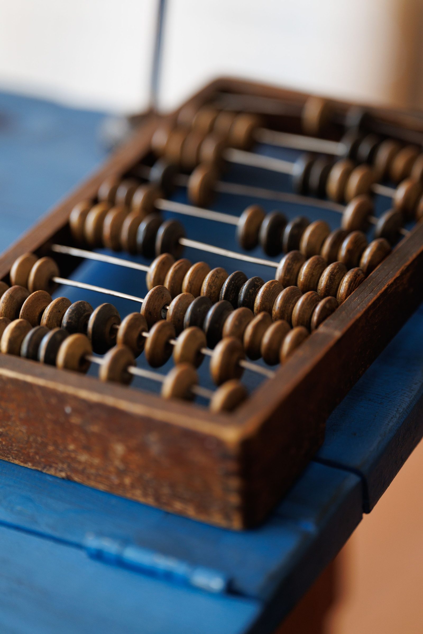 A wooden abacus with rows of counting beads rests on a blue table.