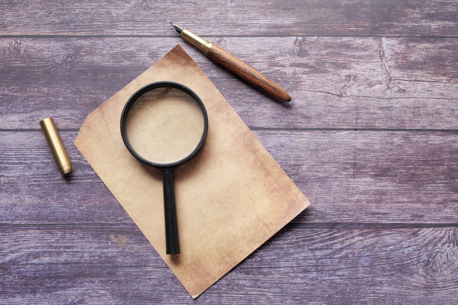 A magnifying glass and a quill pen on a blank sheet of paper on a wooden table.