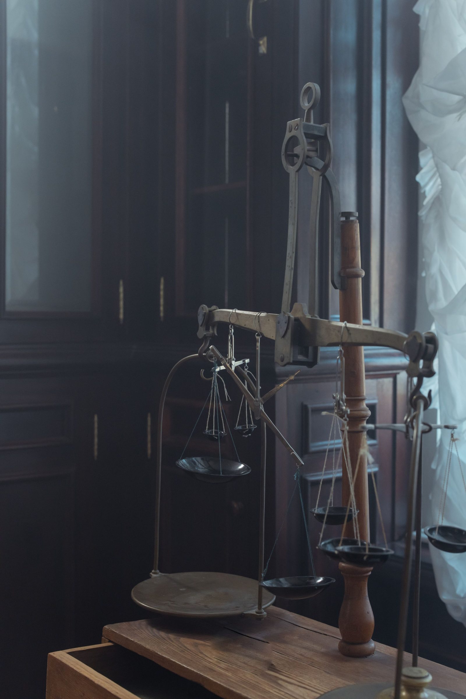 A vintage brass balance scale standing on dark wooden furniture in a dimly lit room.