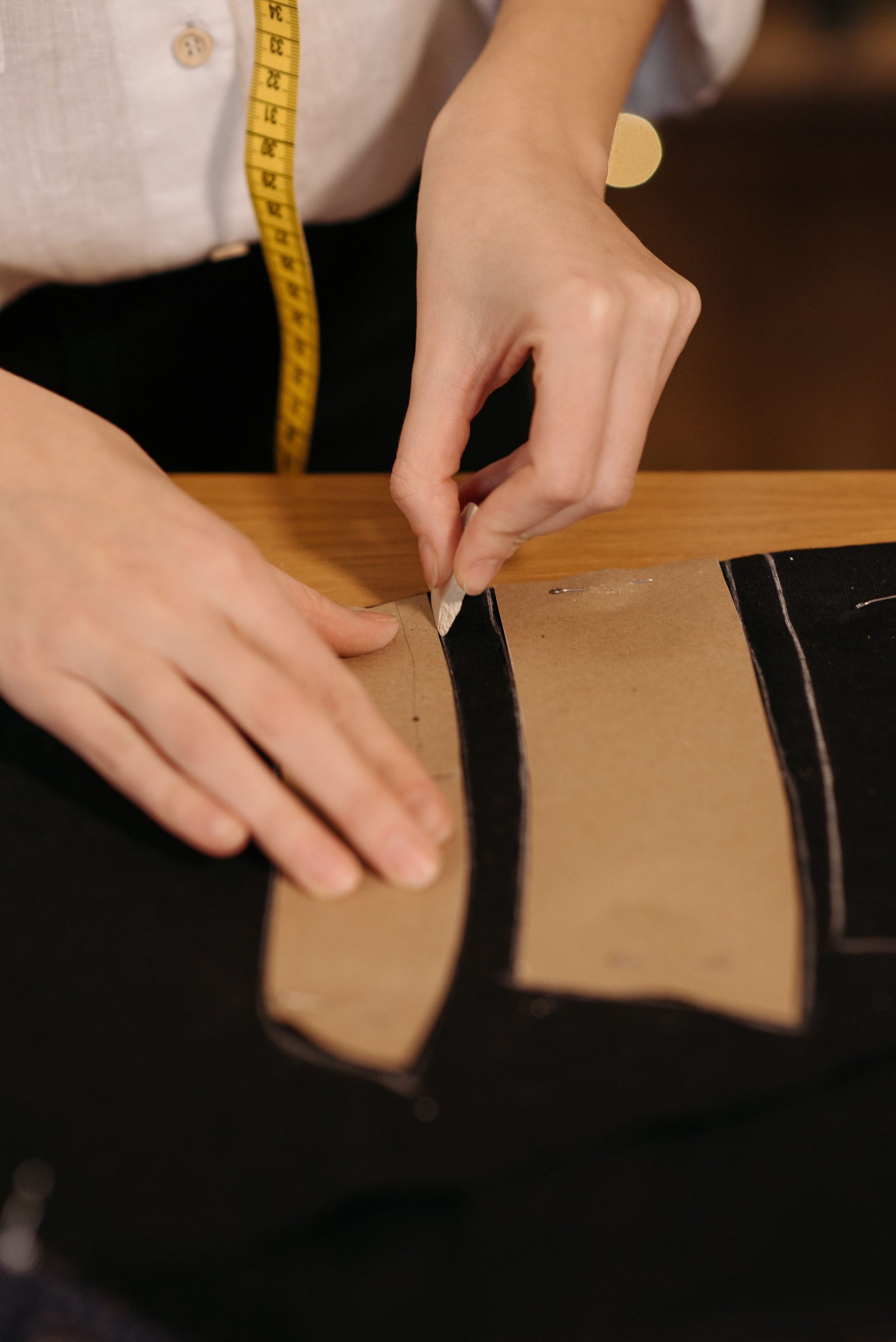 A tailor’s hands trace the outline of a pattern piece in chalk on black fabric.