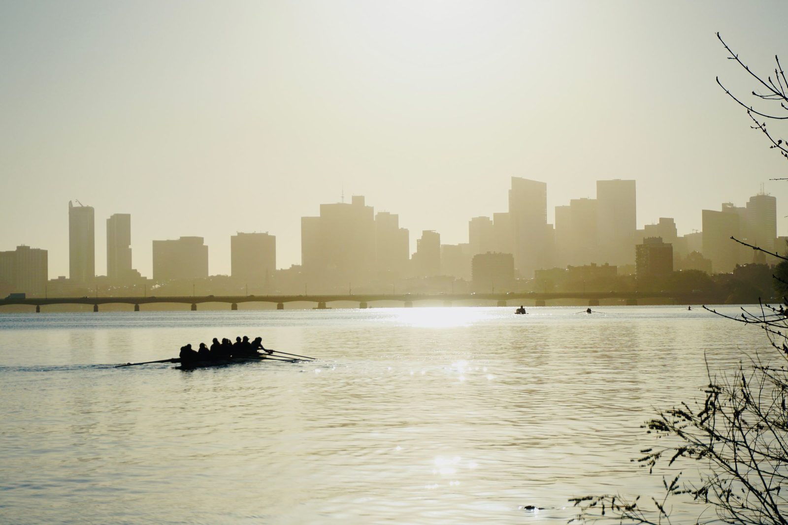 A rowing crew in silhouette on a calm lake with a city skyline behind in haze.