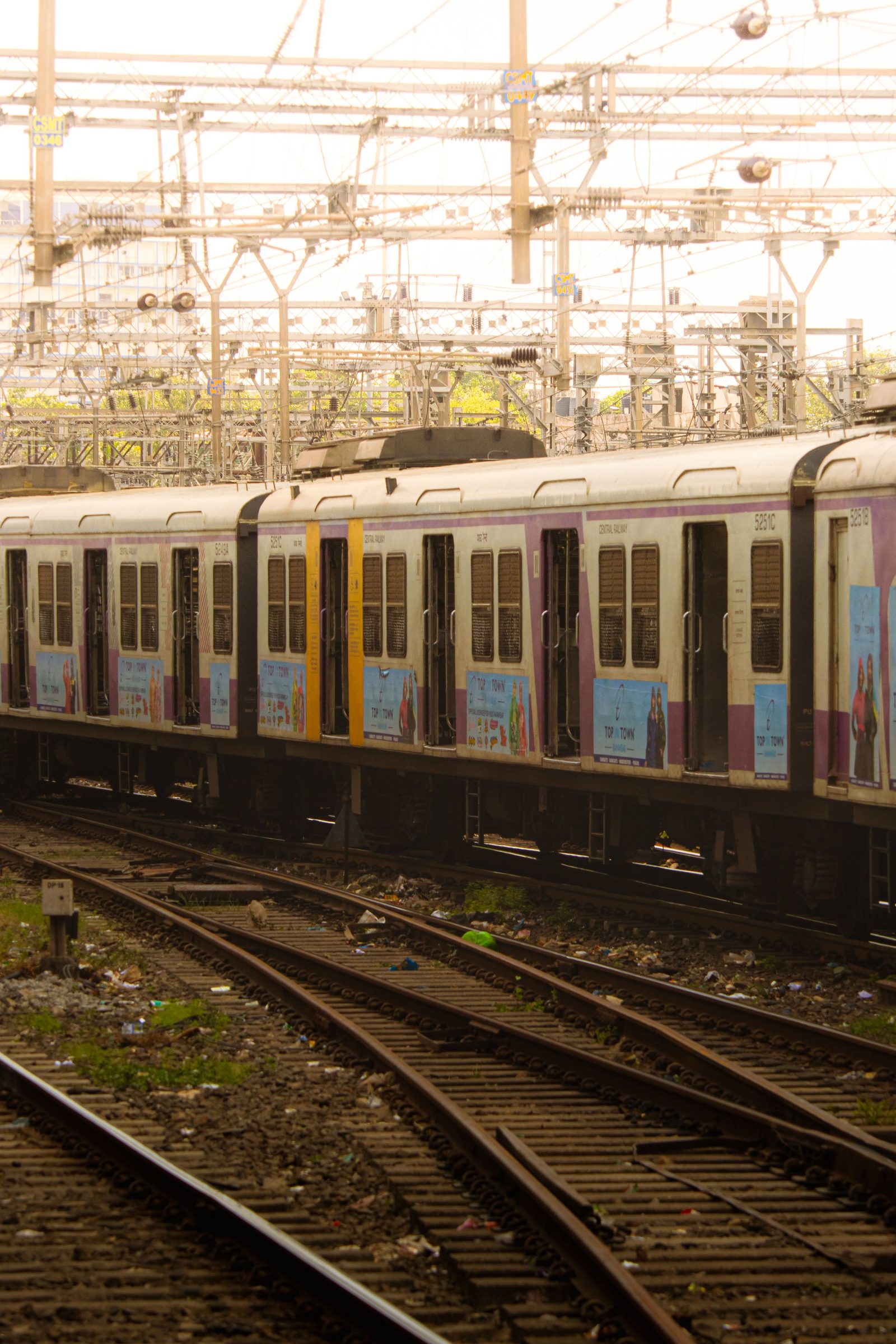 A Mumbai local train running on tracks under overhead power lines.