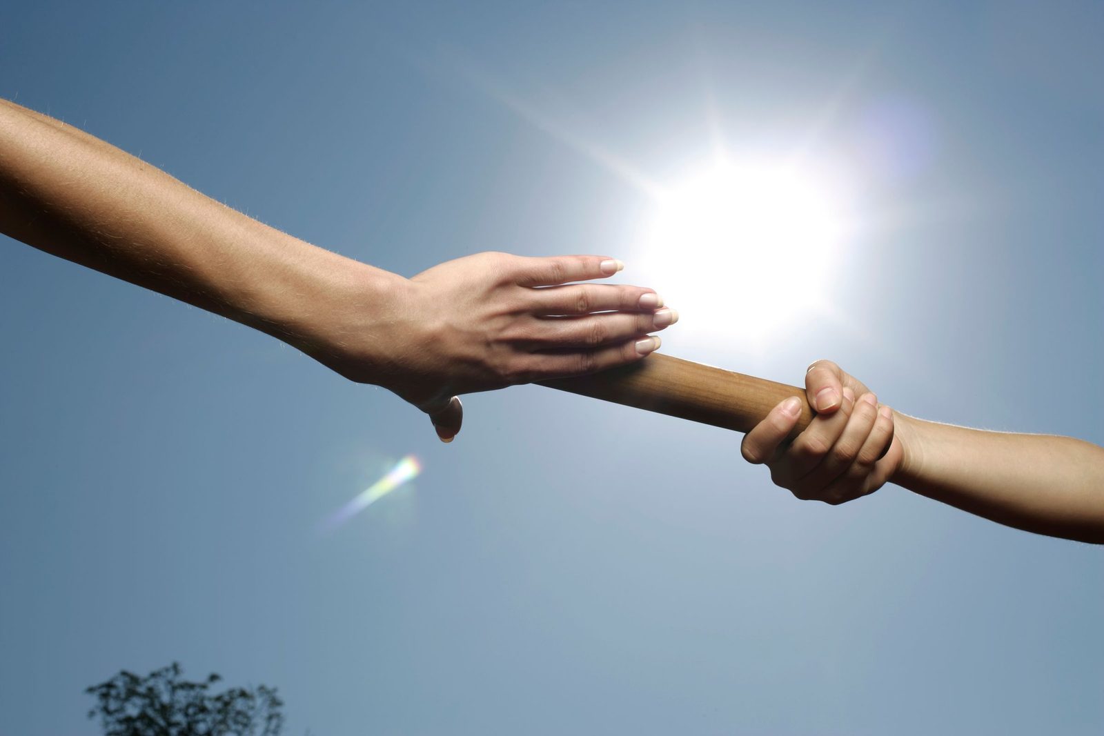 Two hands holding a relay baton between them against a bright sky.