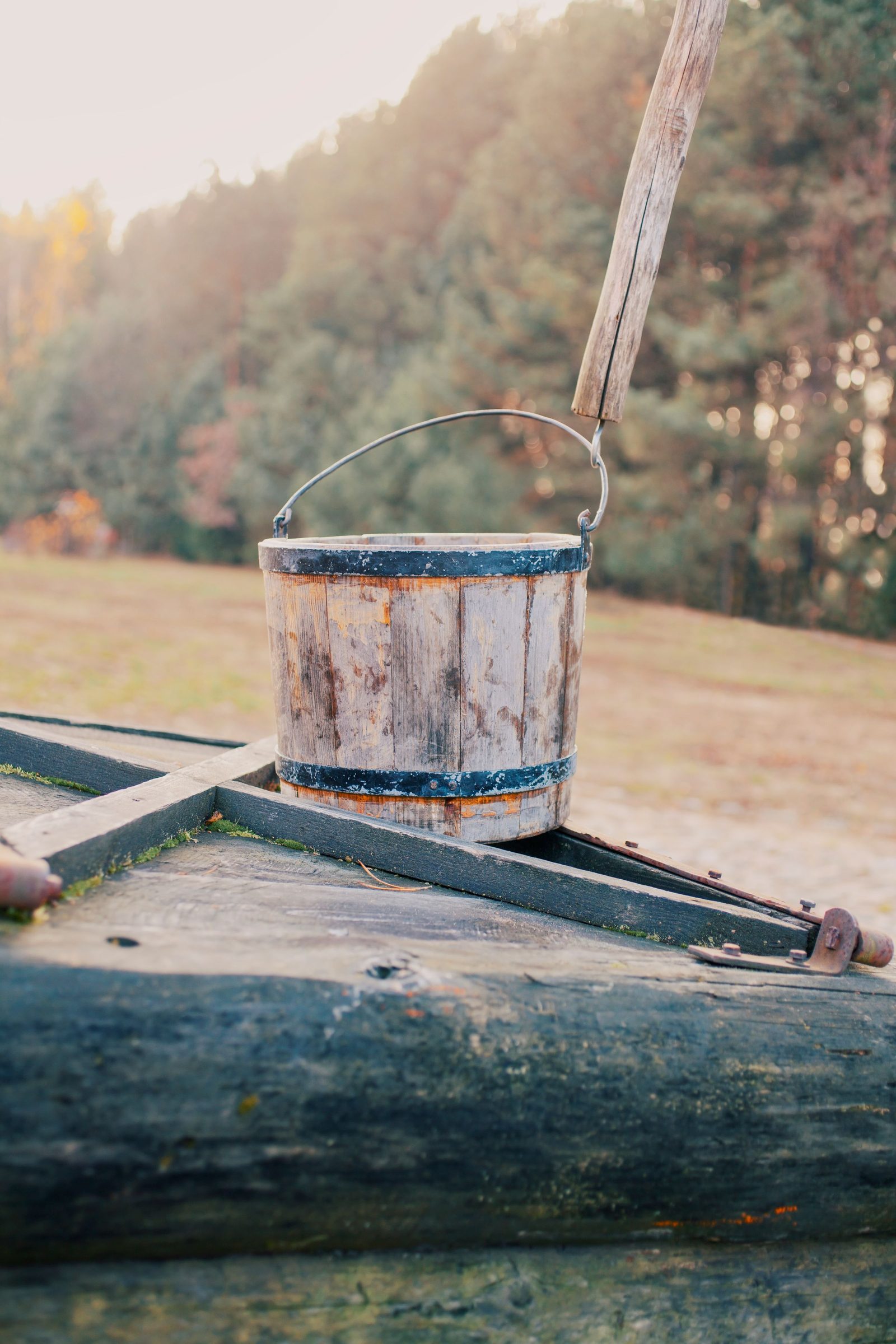 An old wooden bucket rests on the rim of a countryside well.