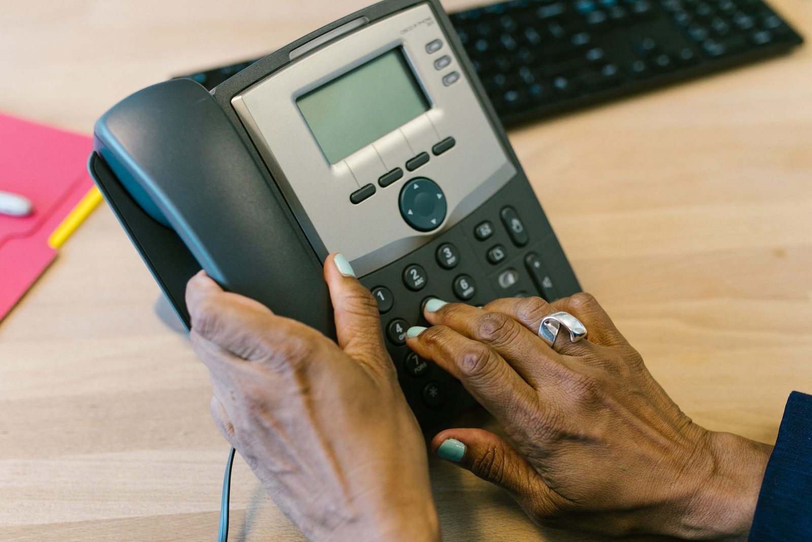 Hands dial a desk telephone in an office.