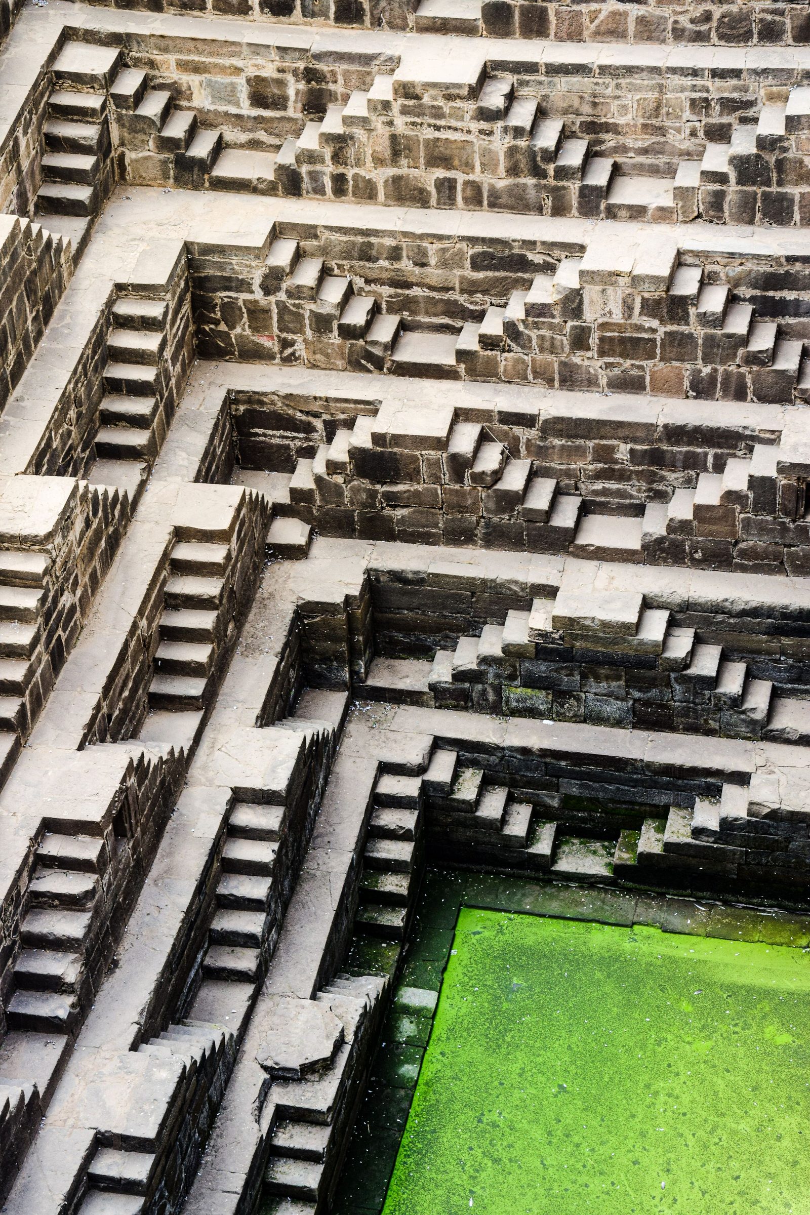 Aerial view of a stone stepwell with flights of stairs descending to green water.