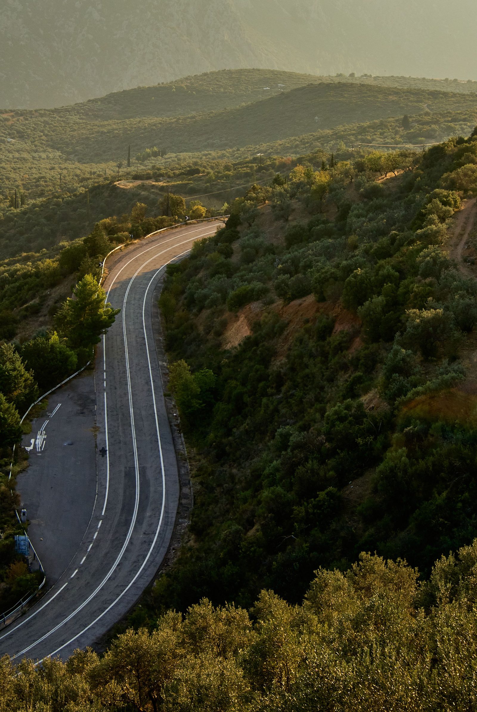 A mountain road twists through green slopes under a golden evening sky.