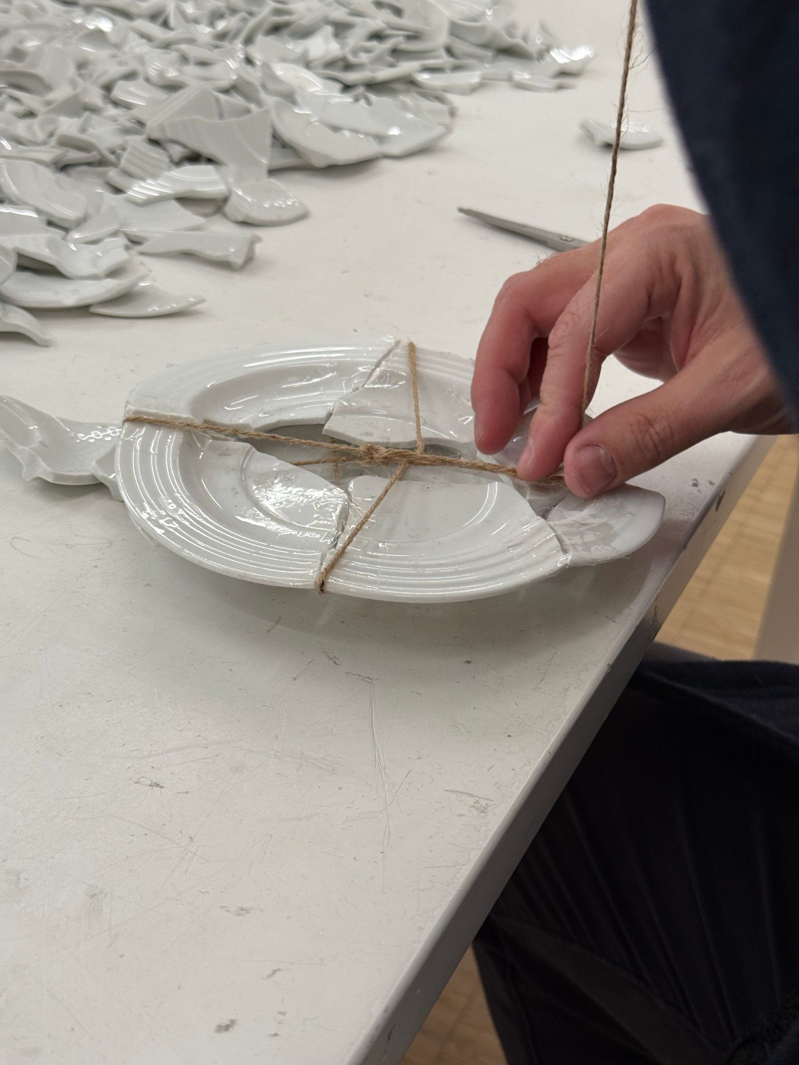 Hands bind the broken pieces of a plate together with twine in a workshop.