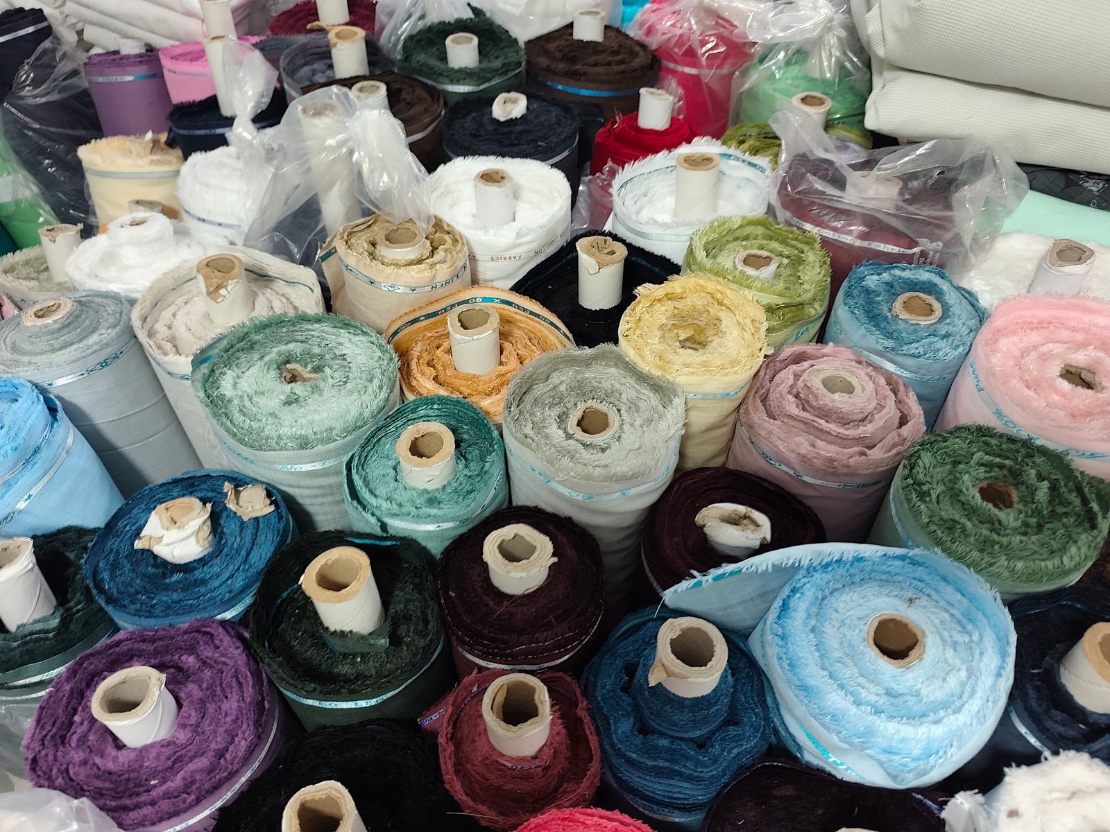 Rolls of fabric in many colours are stacked on the shelves of a textile shop.