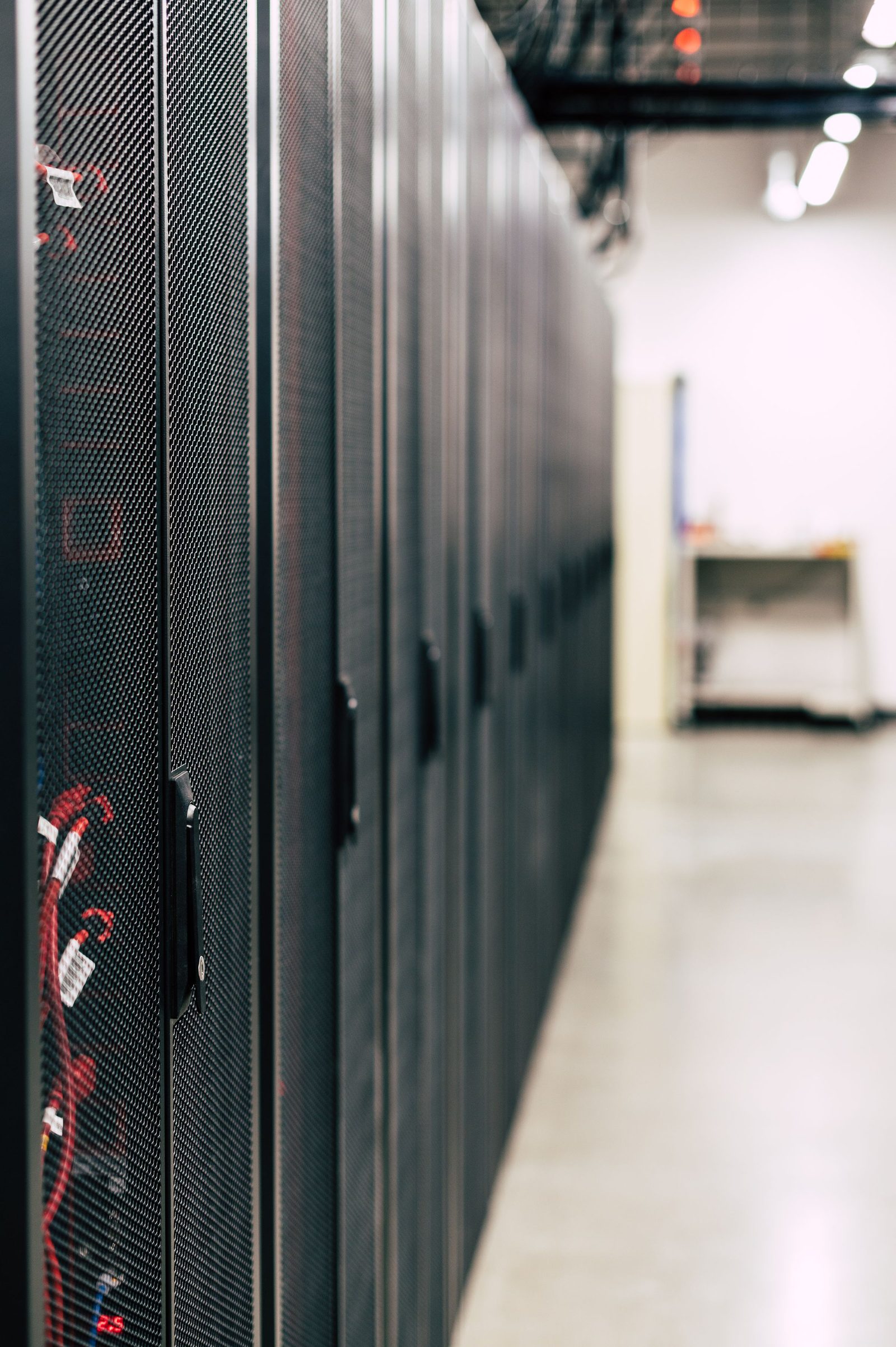 A row of black server cabinets with red cables in a lit data centre.