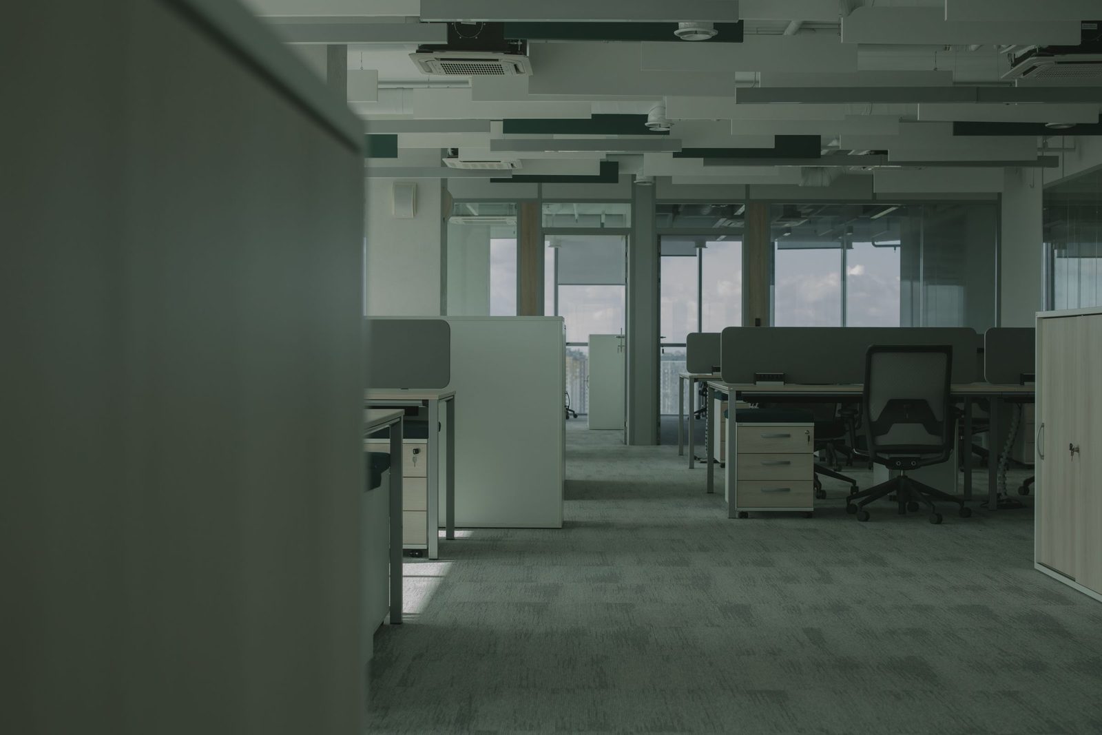 An empty open-plan office with rows of desks chairs and partitions.