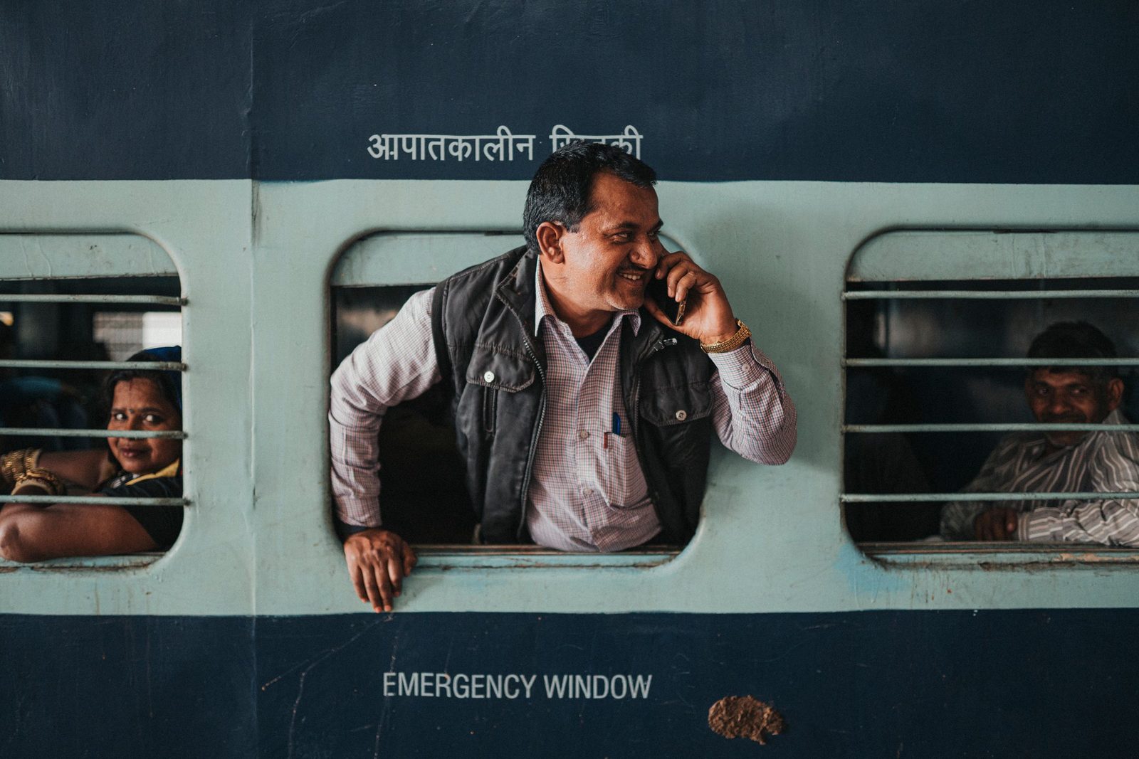 A man leans at the window of a train in Jaipur and talks on his mobile phone.