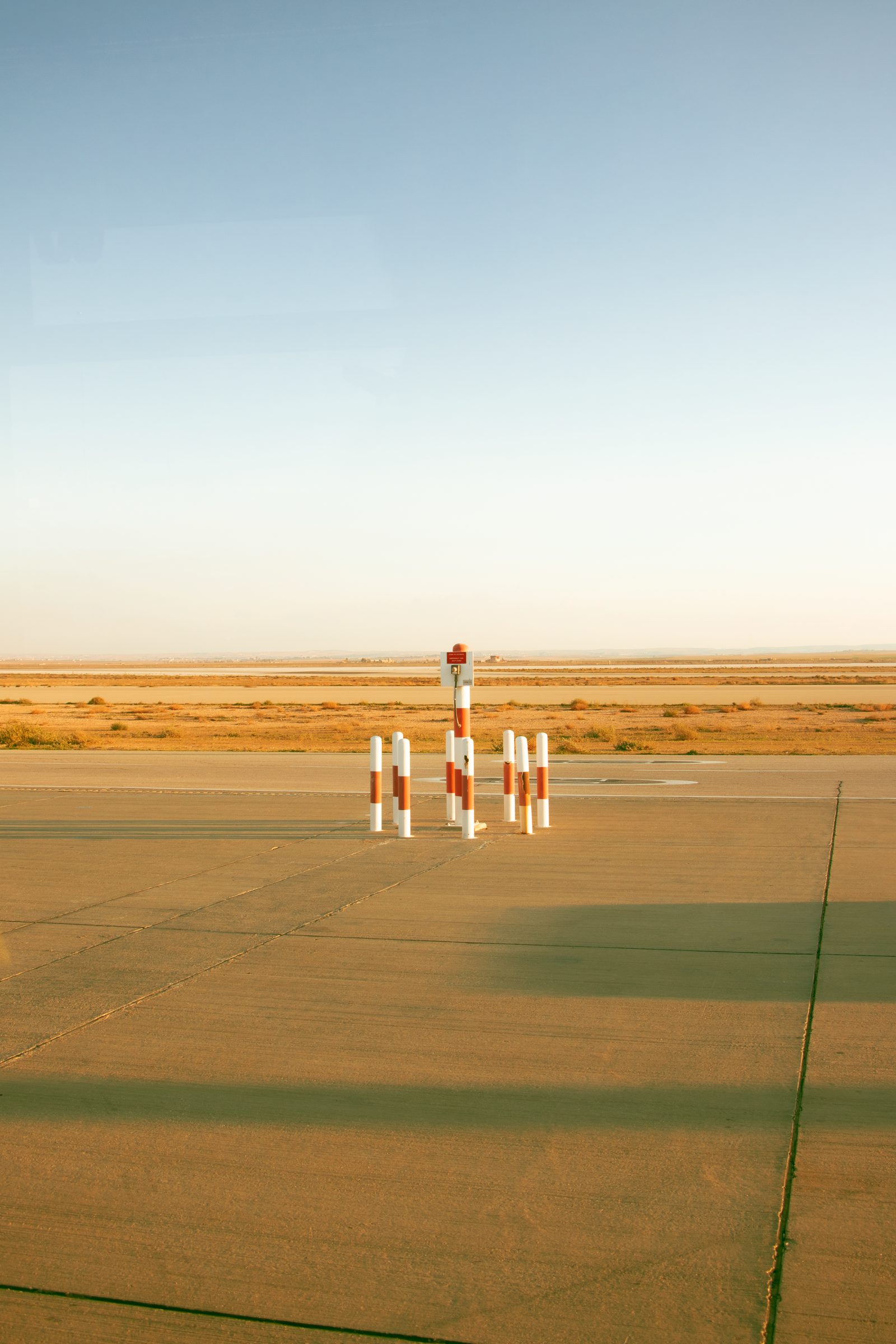 An empty runway runs into a flat desert under an overcast sky.