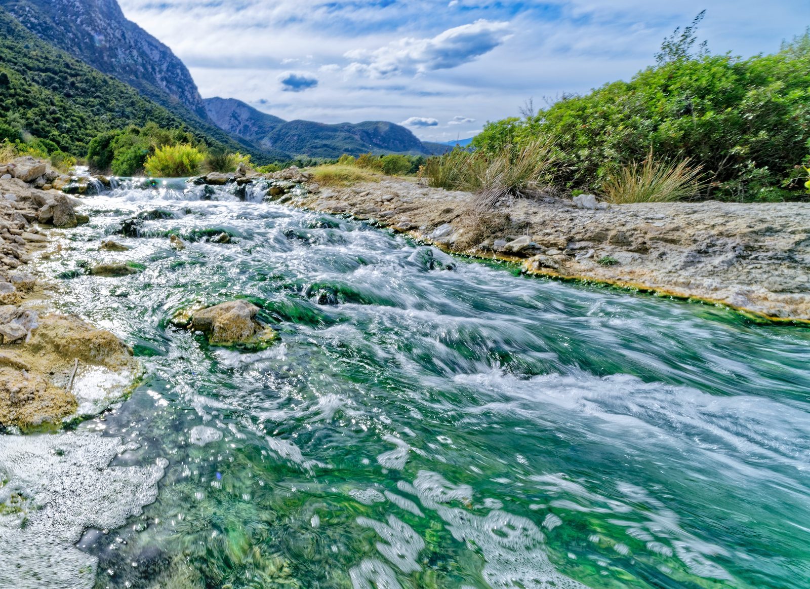 A stream running between rocks below steep green mountains at Thermopylae