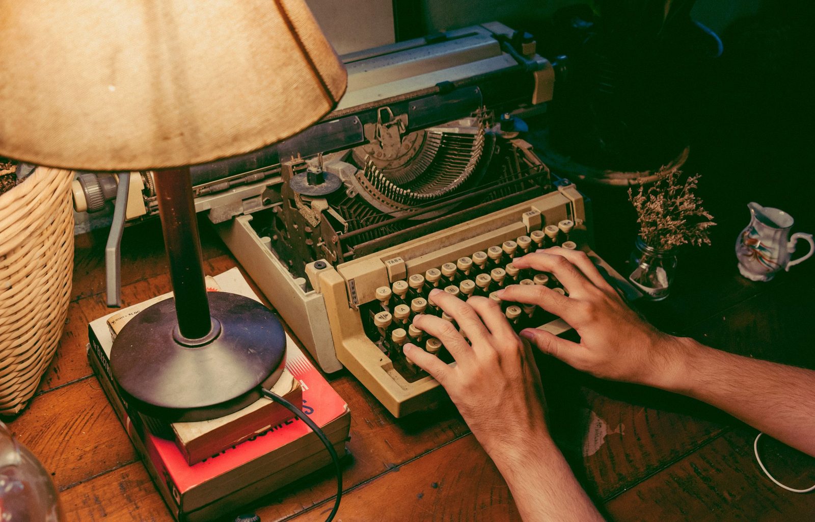 Hands typing on a vintage typewriter under the glow of a lamp.