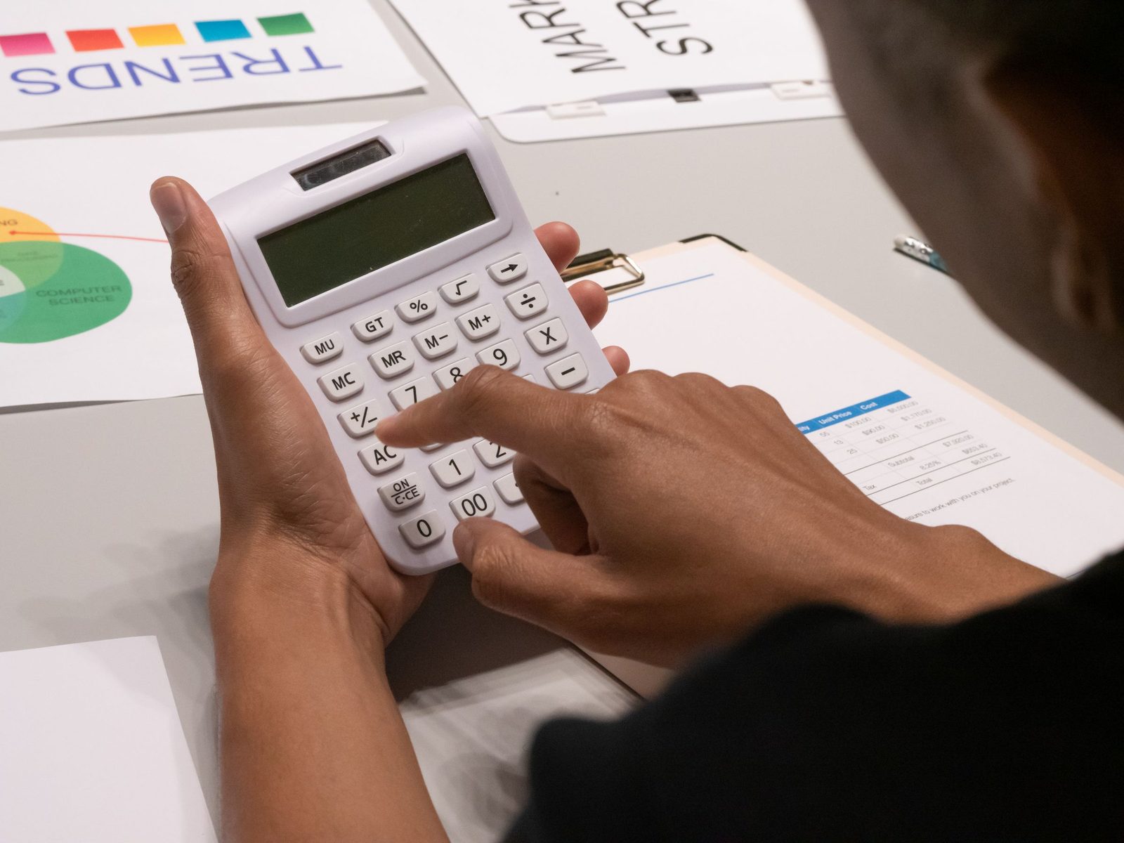 Hands working a calculator over printed financial papers.