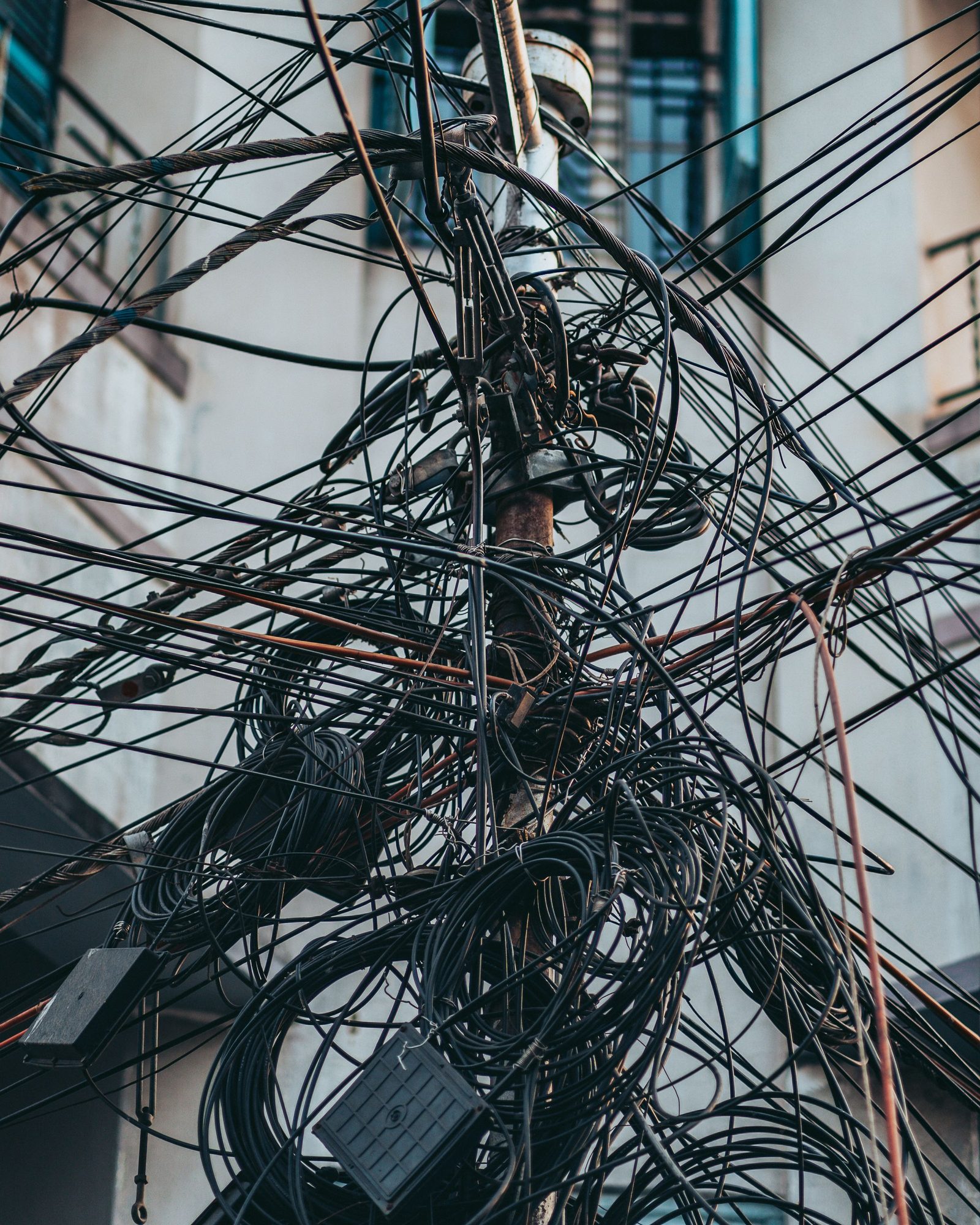 A chaotic tangle of electricity wires gathered on a utility pole above a city street.