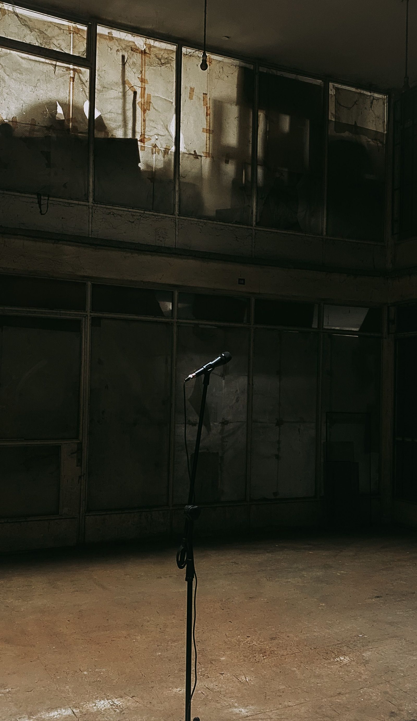 A lone microphone on a stand in a dark disused hall.