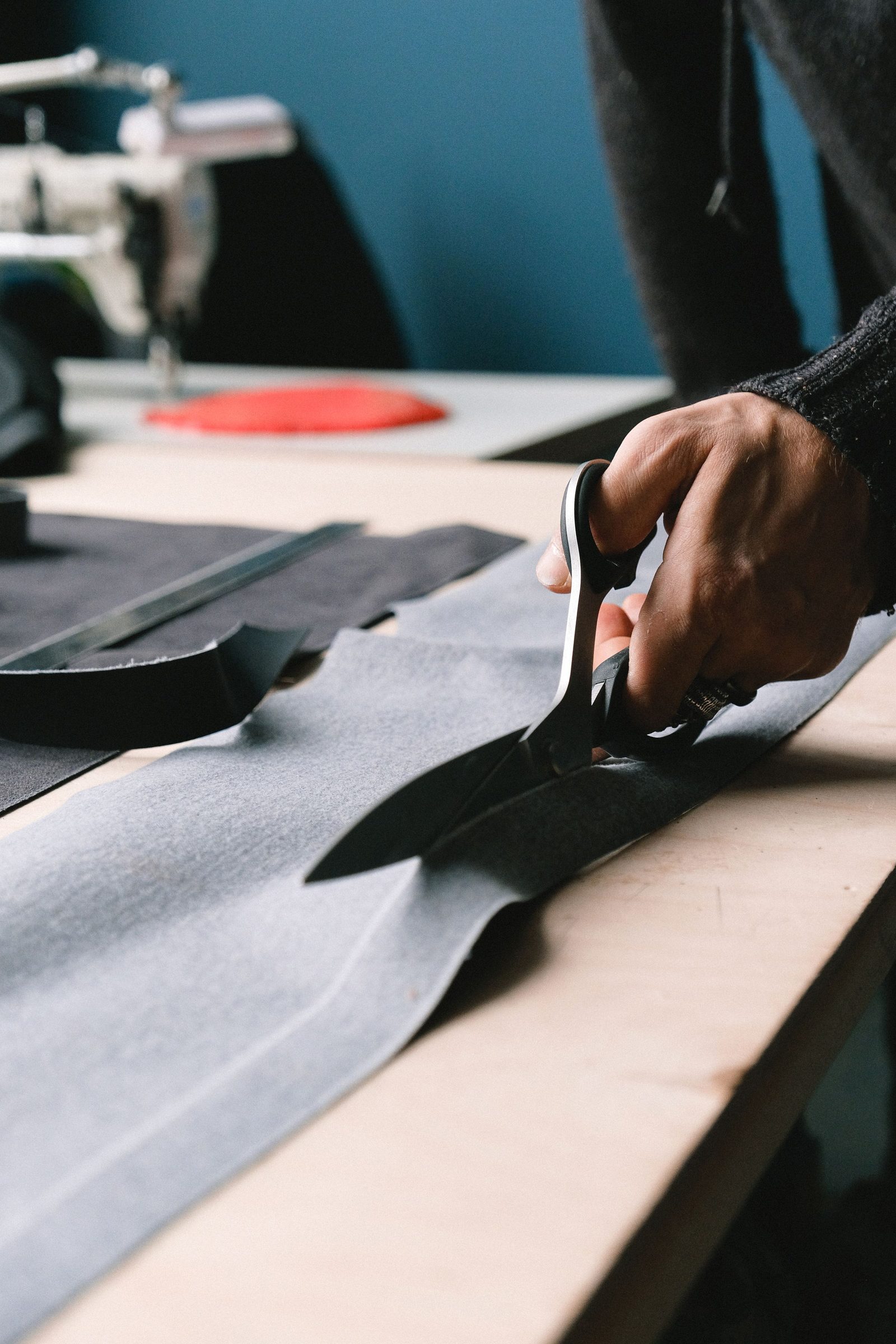 A hand cuts fabric with tailor’s scissors on a workbench.