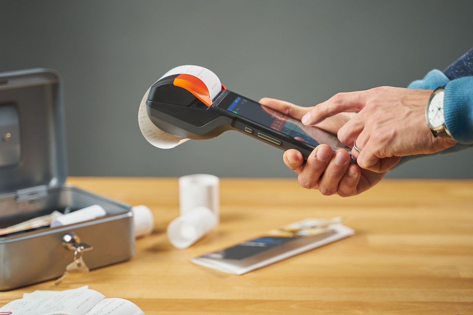 Hands operate a small receipt printer on a wooden table.