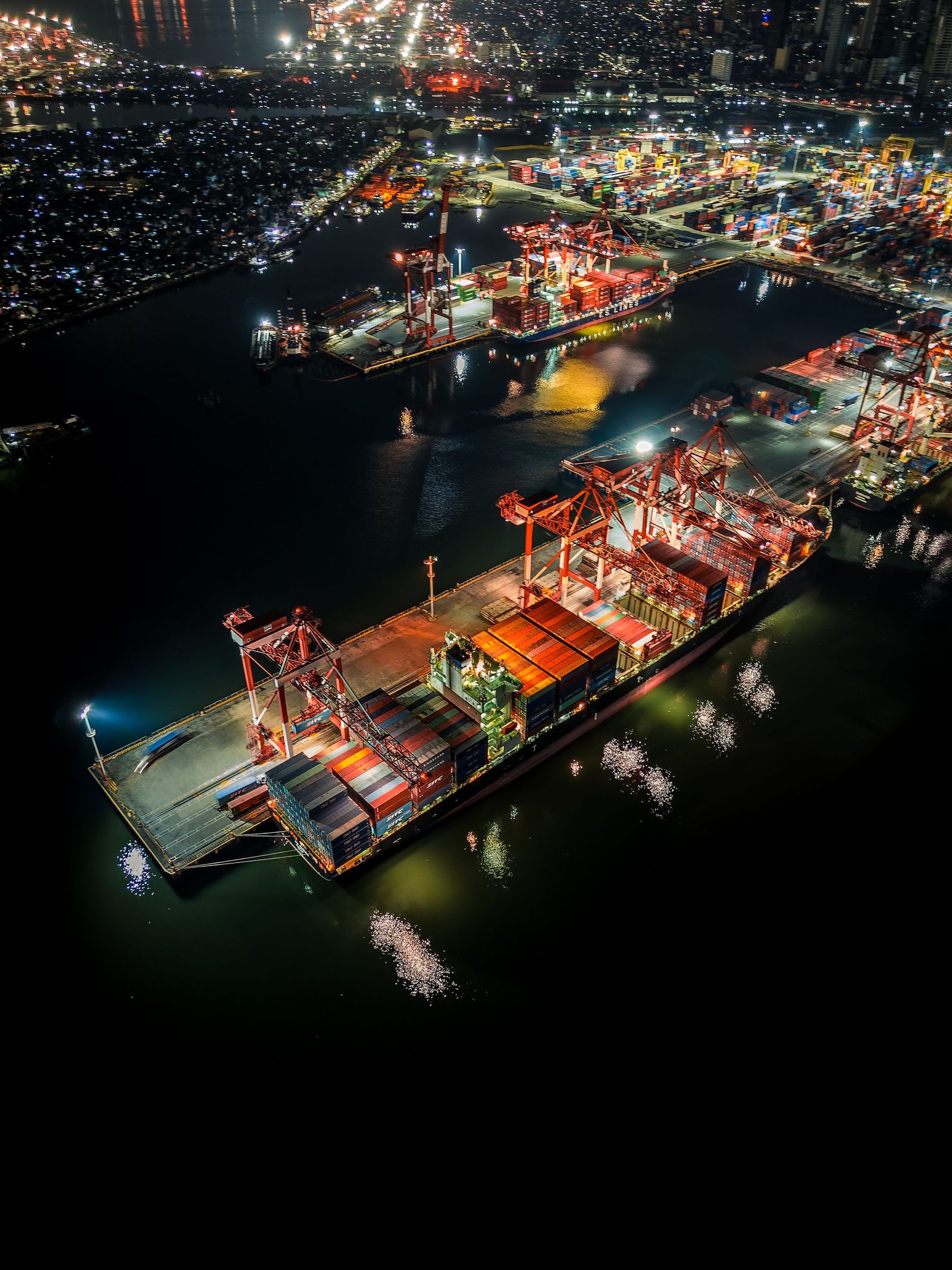 An aerial view of a container port lit up at night beside a city.