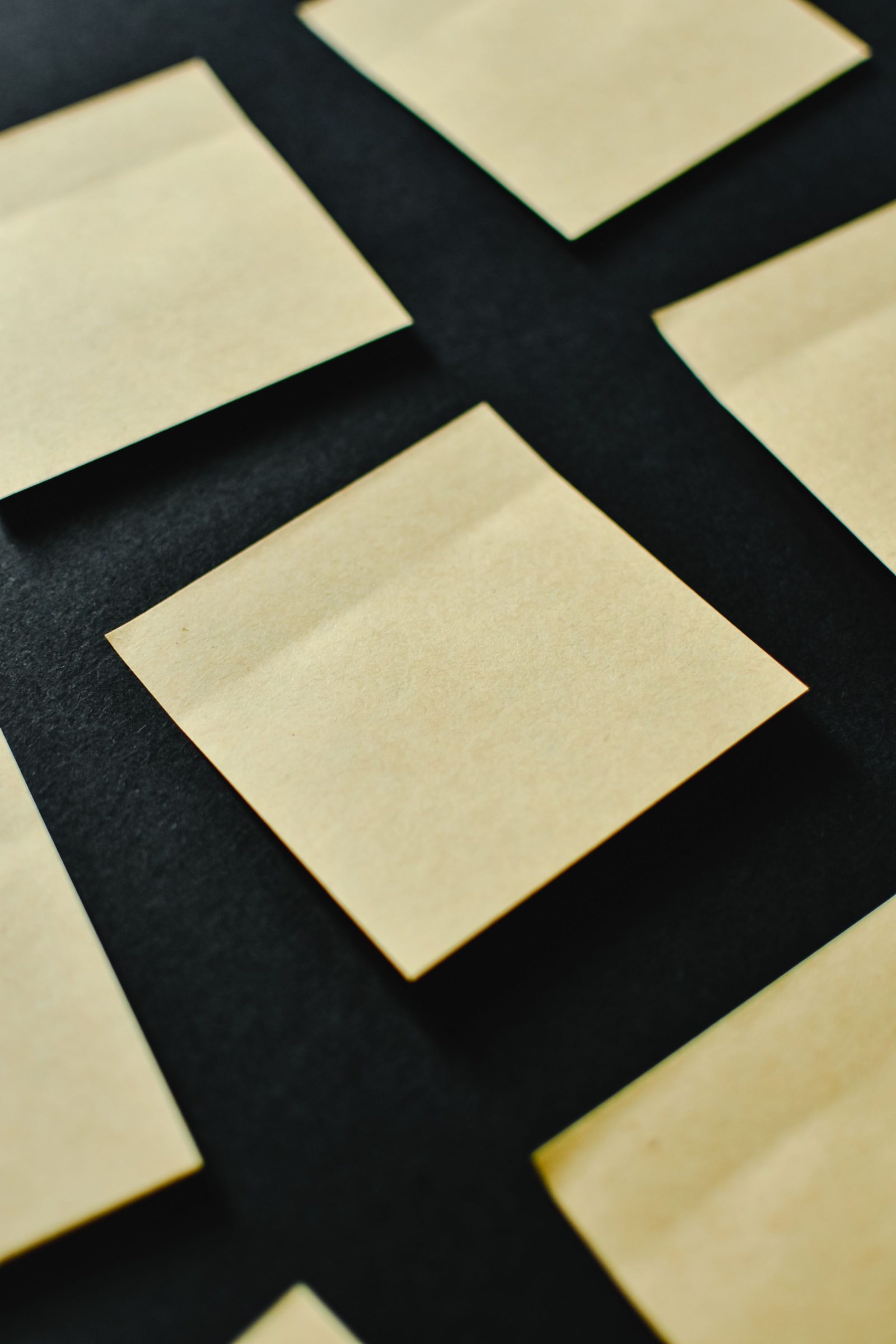 Blank sticky notes in several colours laid out on a black surface.
