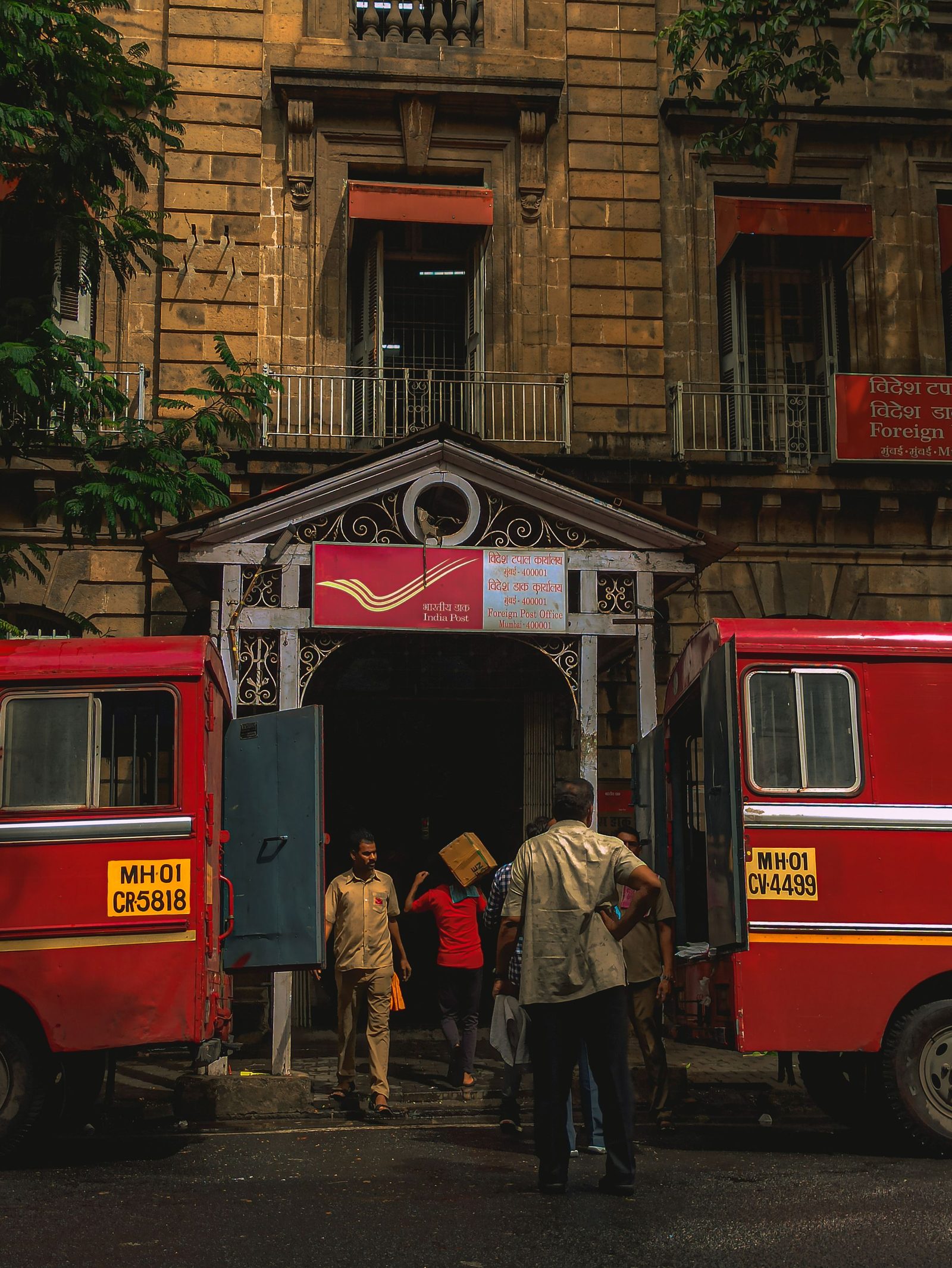 Postal workers beside red mail vans outside a colonial-era post office building in New Delhi.