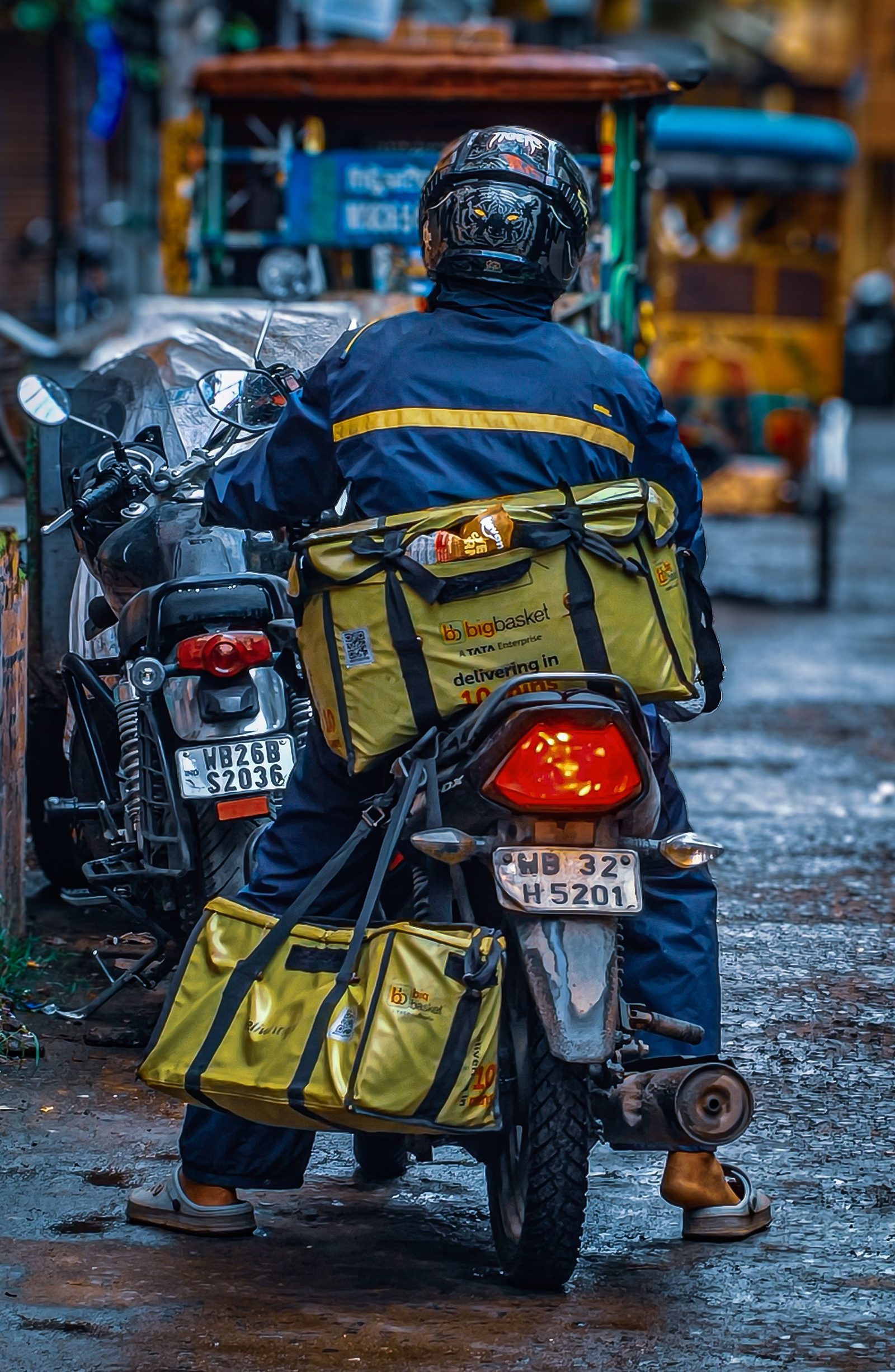 A delivery rider on a motorbike moves through a wet city street in India in the rain.