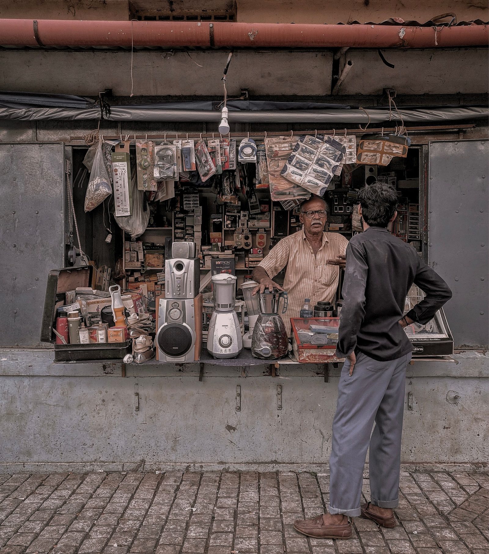 A vendor and a customer at a sidewalk electronics stall in Thalassery.