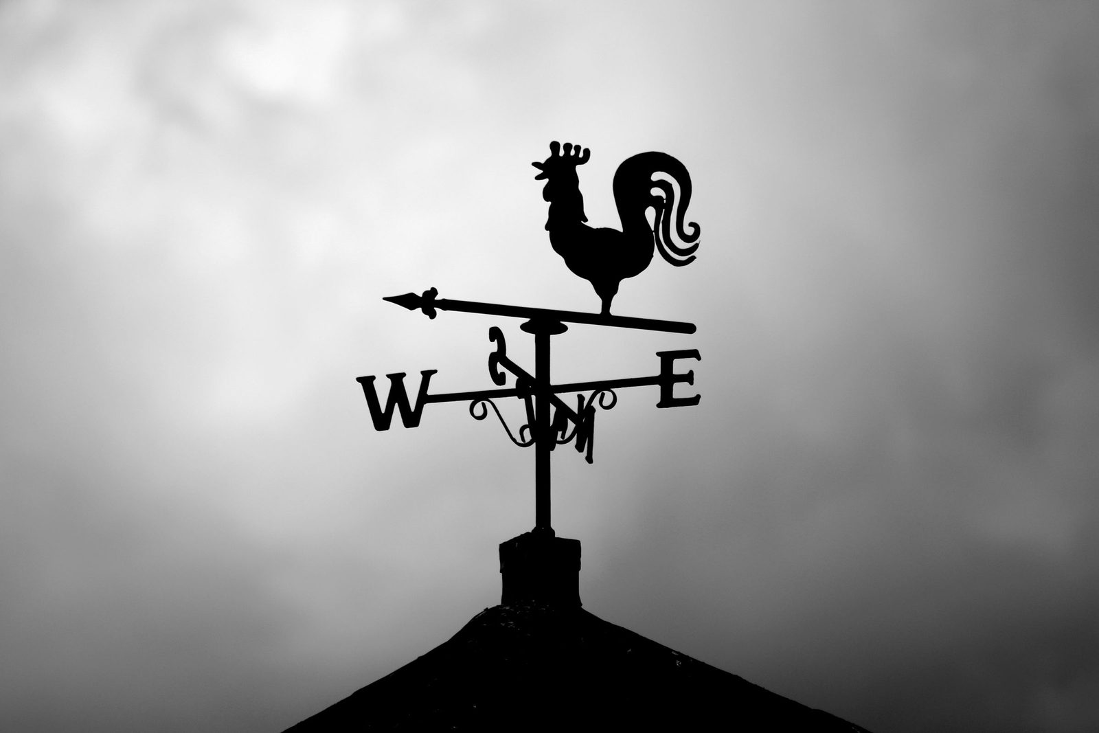 The silhouette of a rooster weather vane against a cloudy sky.