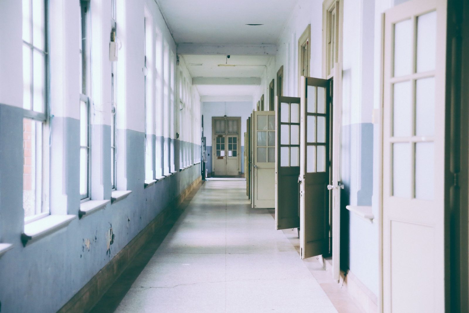 A bright empty corridor with a row of open doors on one side.