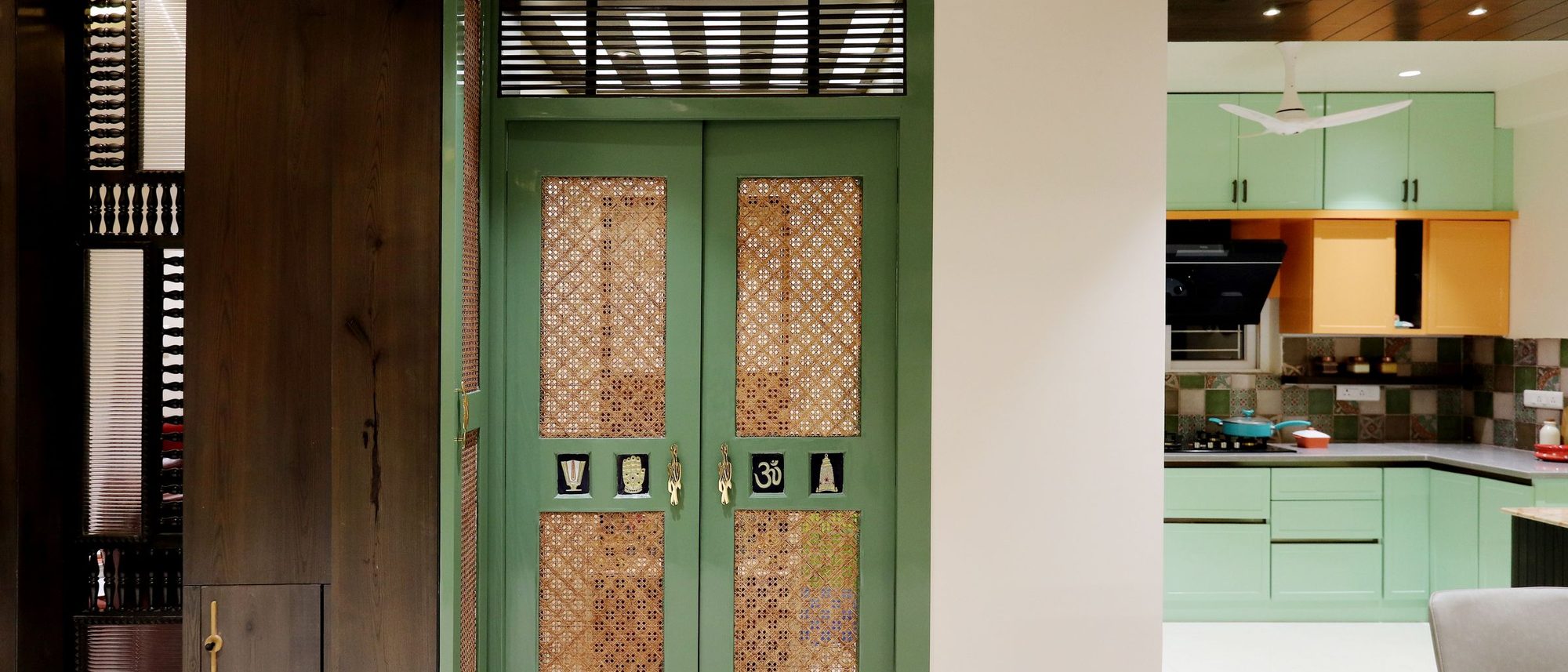 A carved doorway in an Indian home opens onto the kitchen beyond.