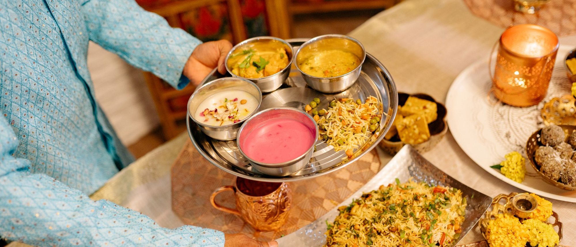 A hand serves food onto a steel thali at a festive family dinner indoors.