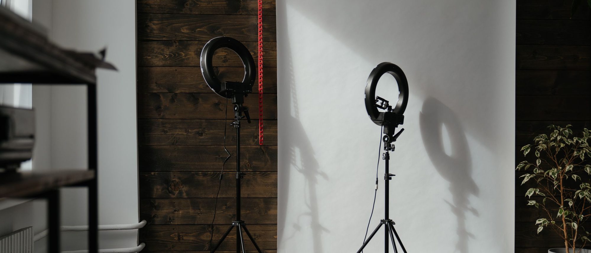 An empty photo studio with ring lights on stands in front of a wooden backdrop.