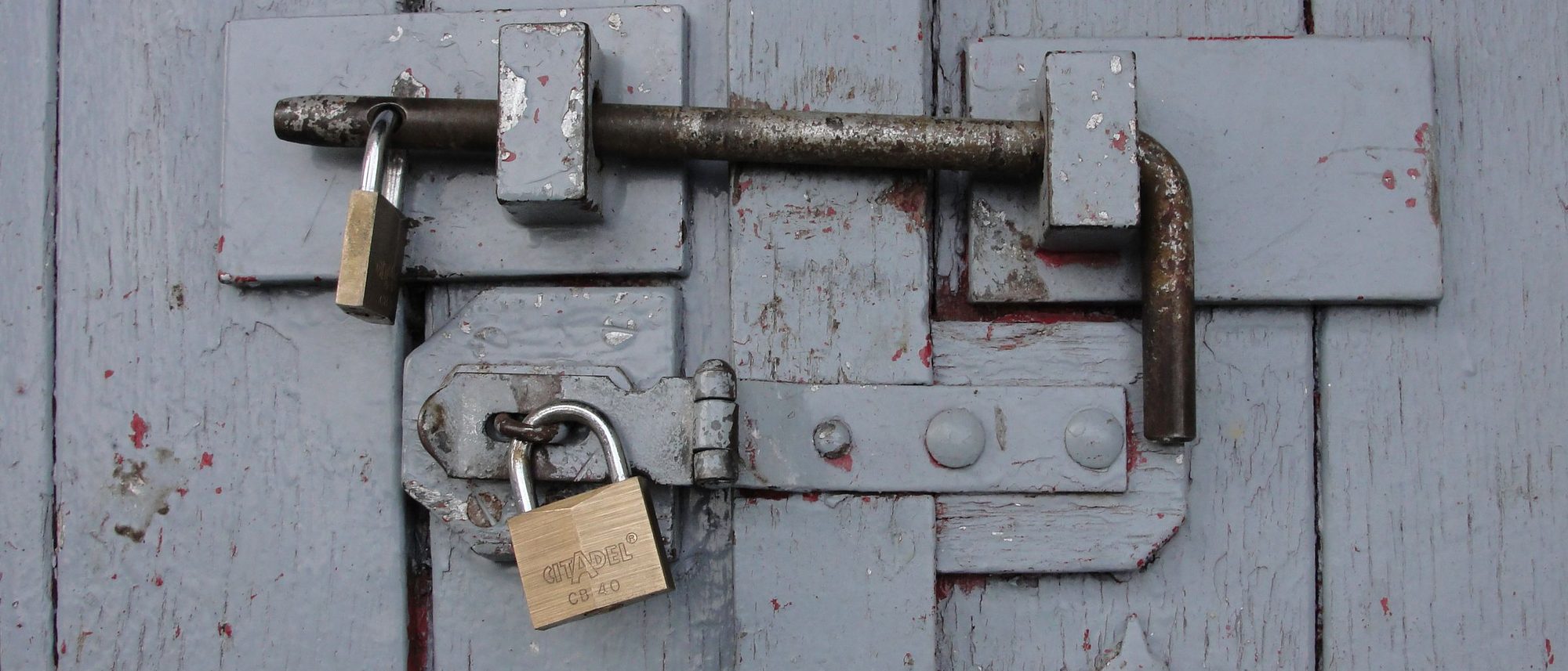 A weathered wooden door barred shut and secured with brass padlocks.